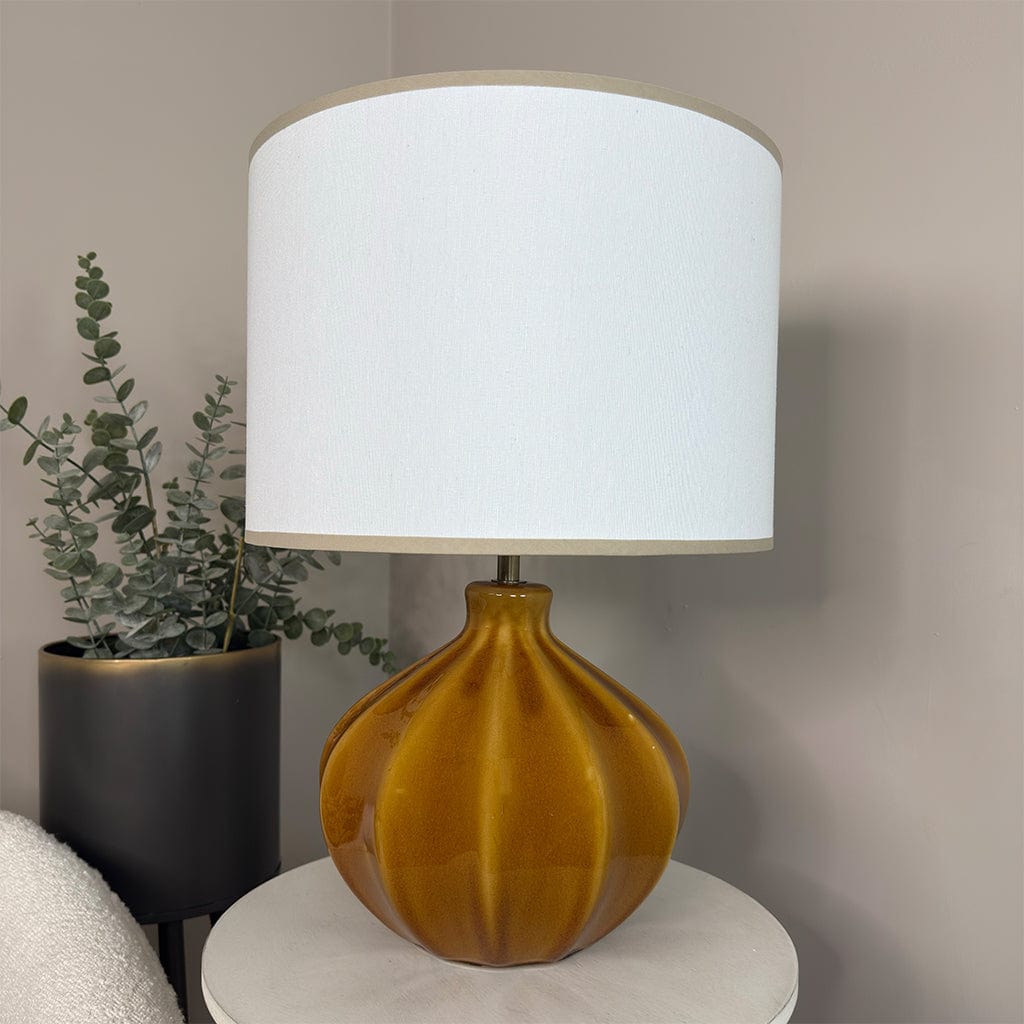 Table lamp with a white shade and brown base next to a plant on a neutral background