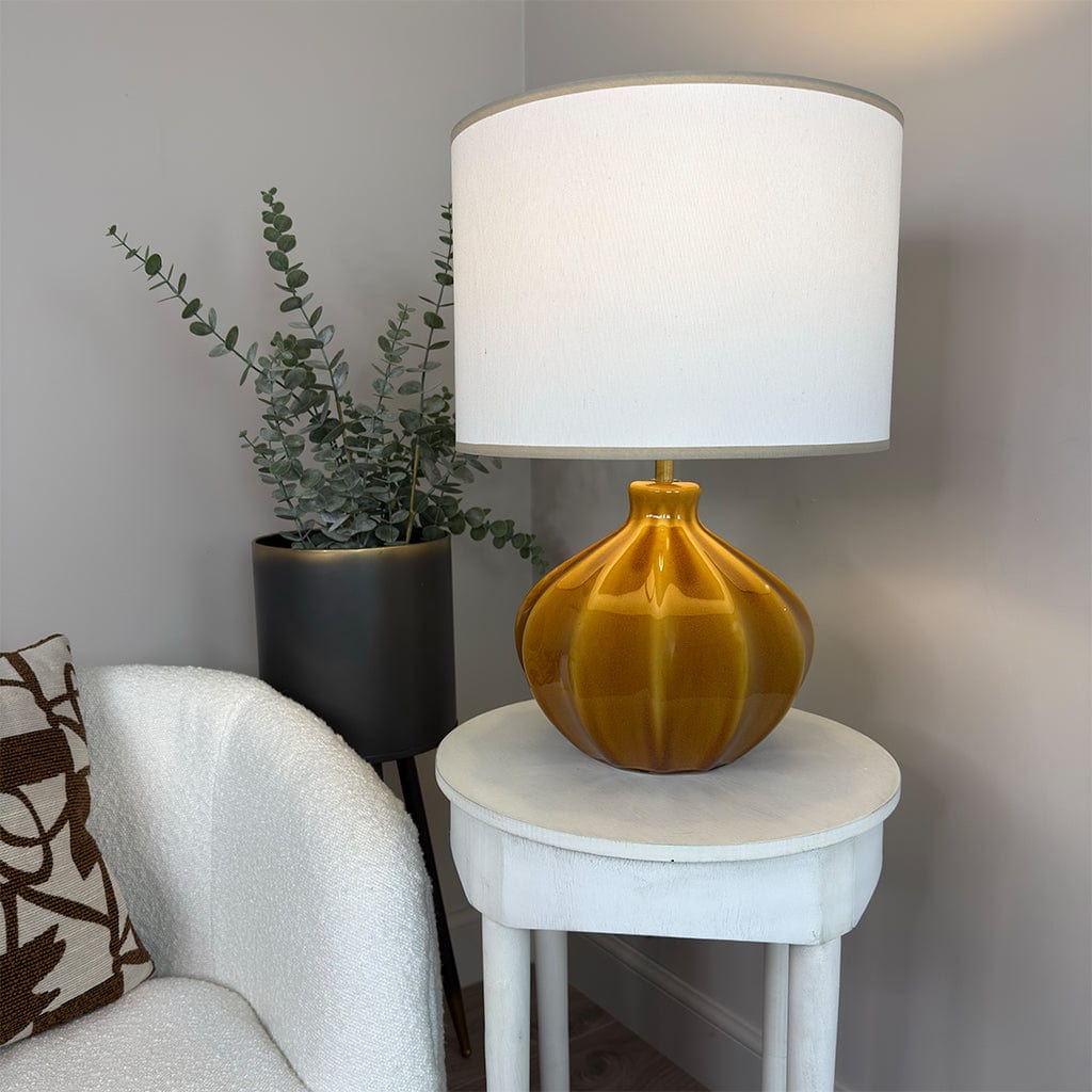 Yellow lamp with white shade on a small round table next to a plant and sofa.