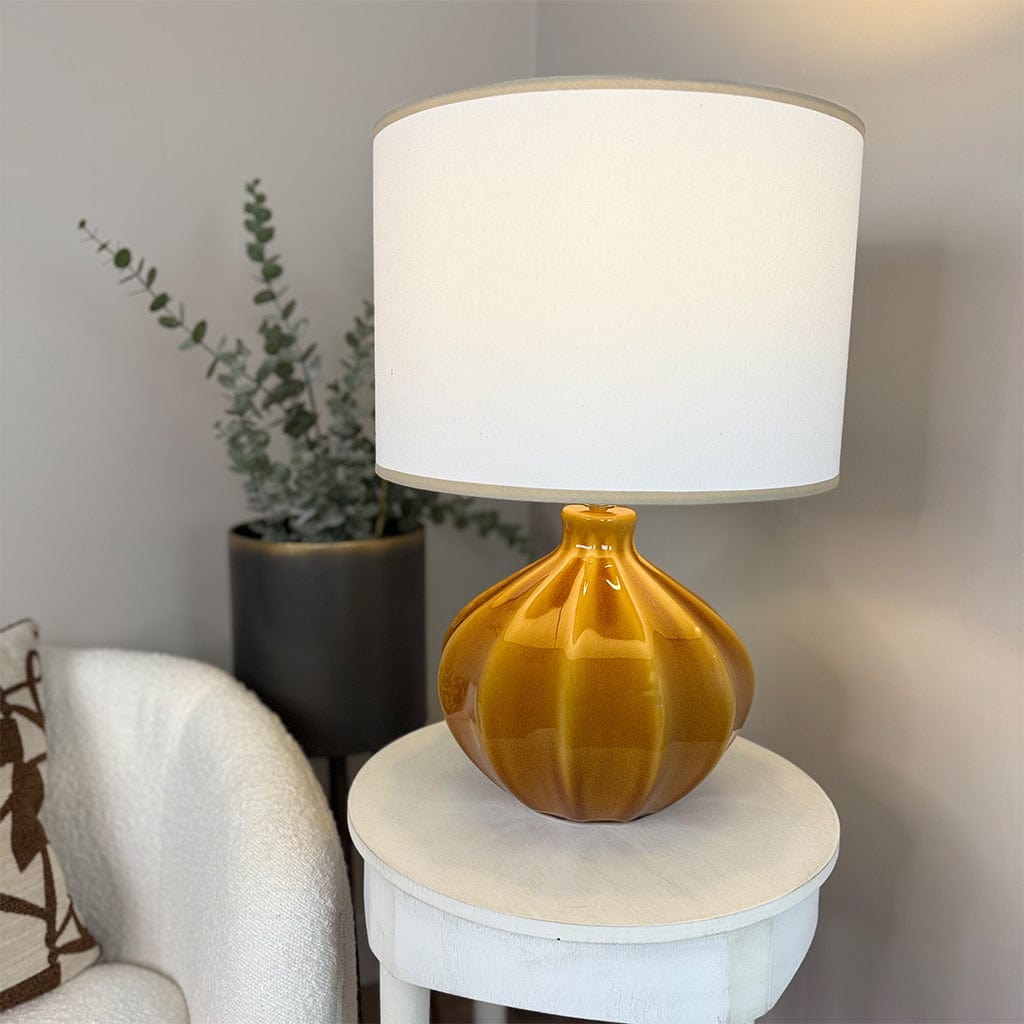 Decorative lamp with a white shade on a small round table next to a chair and plant.