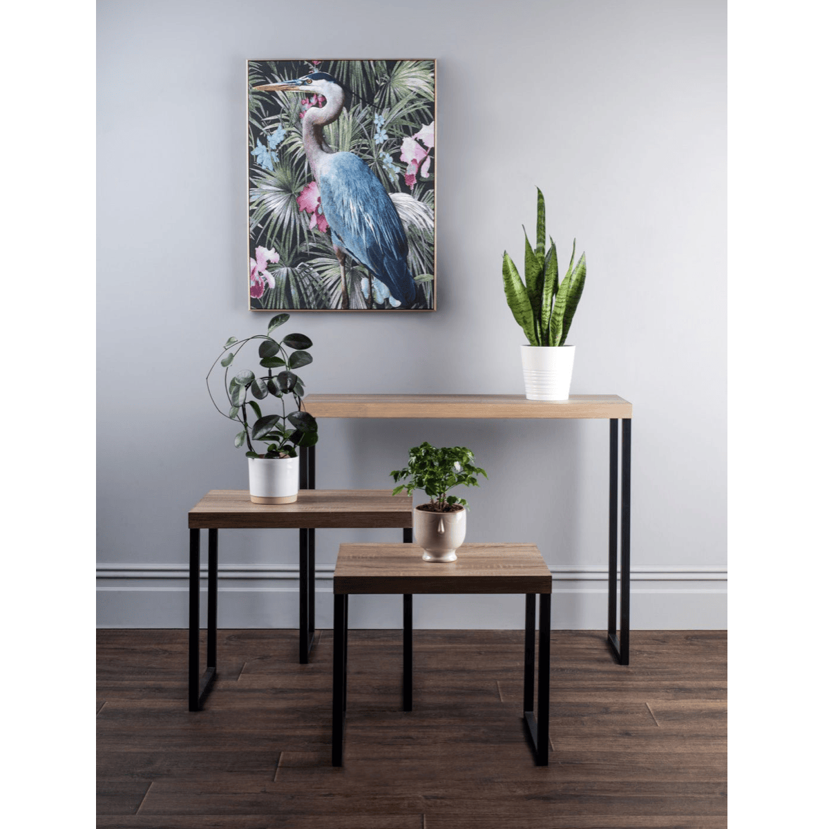 Wooden tables with potted plants and a bird painting on a wall in a room.