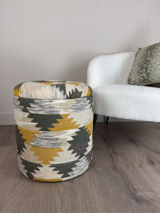 Decorative woven footstool with geometric pattern on a wooden floor next to a white sofa.