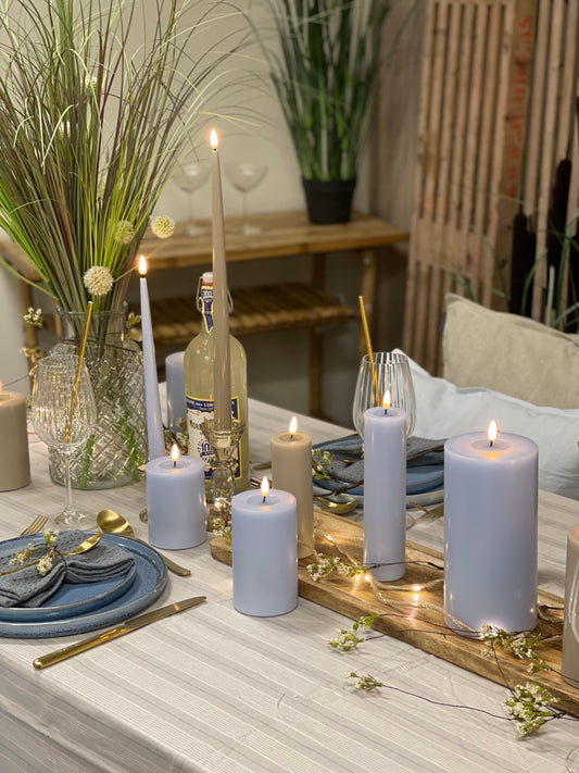 A dust blue LED candle on a table set for a meal, with the glow of the candle illuminating the area.