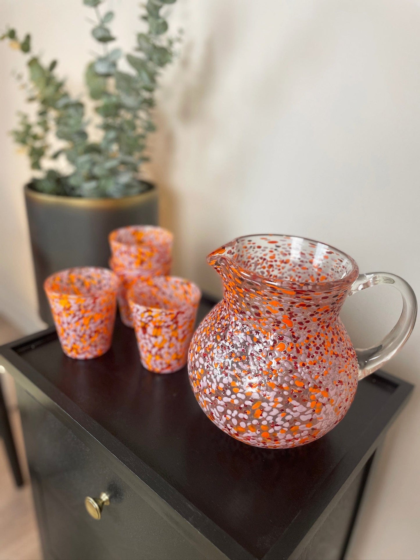 Set of orange and silver speckled glassware on a dark surface with a plant in the background.
