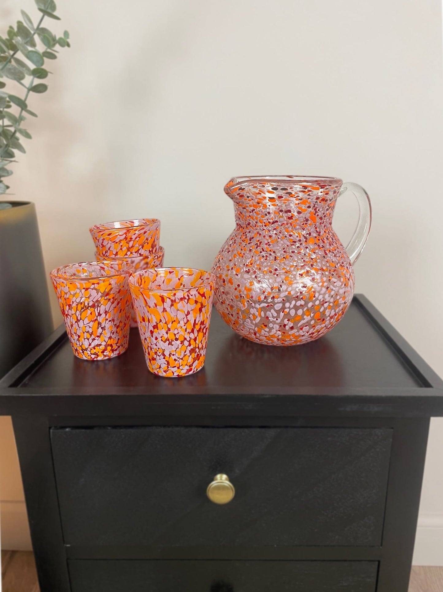 Set of colorful glassware on a dark wooden surface with a plant in the background