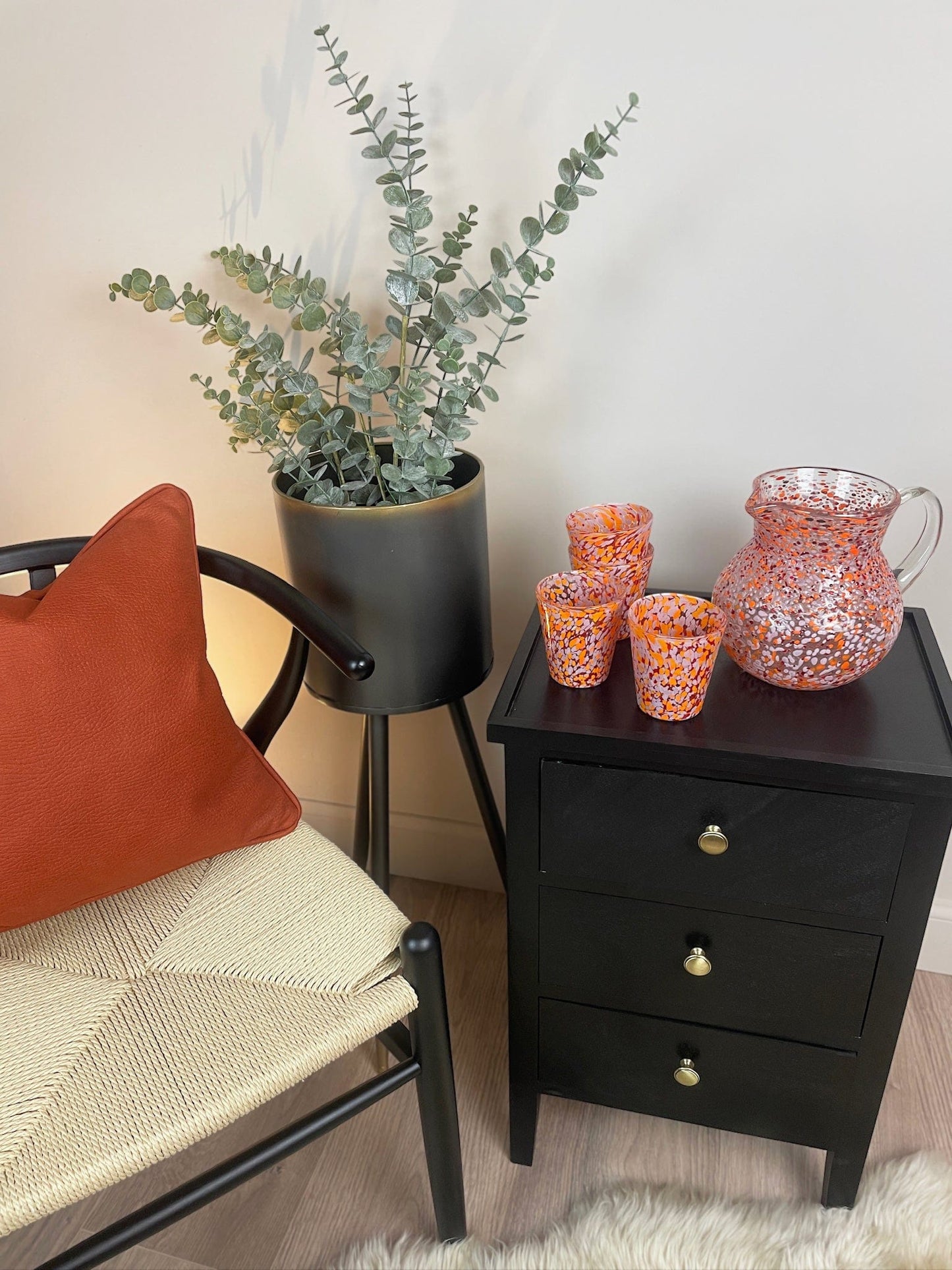 Black nightstand with decorative items next to a chair with an orange pillow