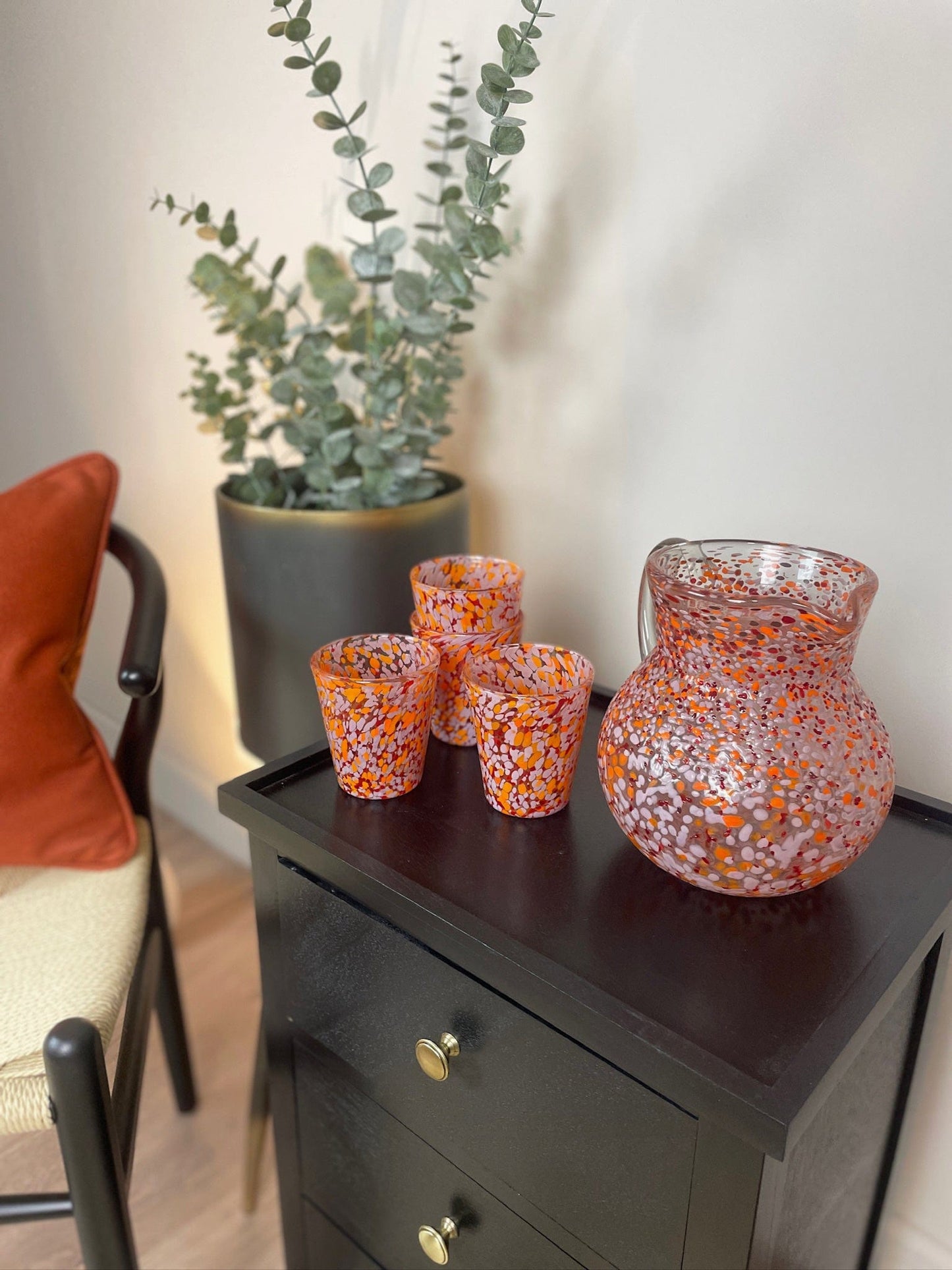 Decorative glass vases on a wooden side table with a plant in the background