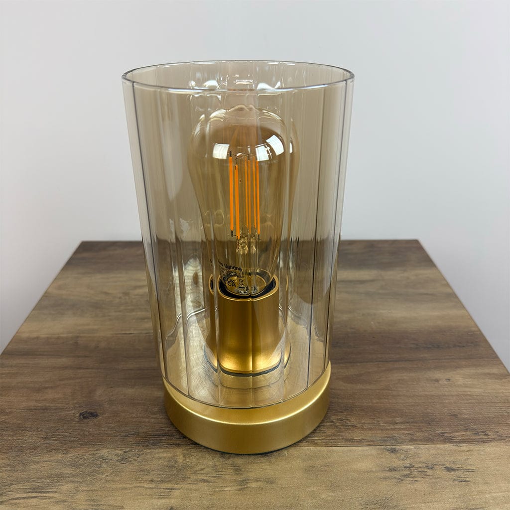 Decorative lamp with a amber glass shade and gold base on a wooden surface.