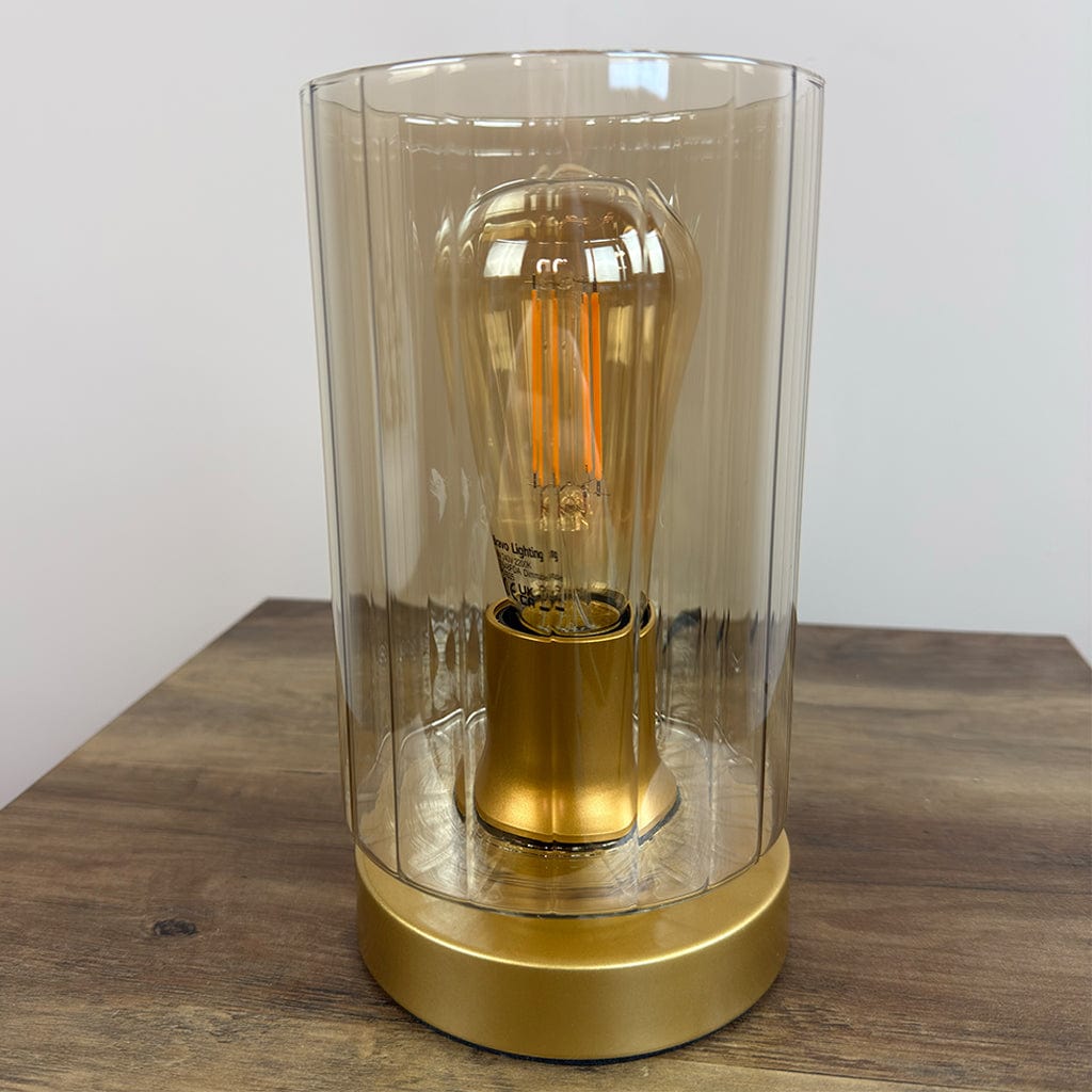 Gold table lamp with amber glass shade on a wooden surface
