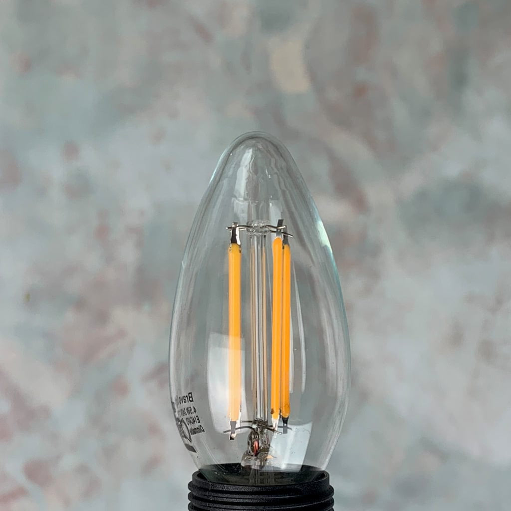 An E14 clear candle non-dimmable LED bulb with visible filaments inside, placed against a textured background.