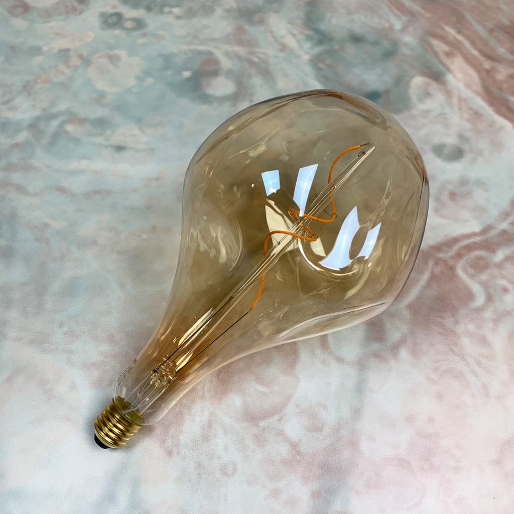 An organically shaped, gold tinted glass LED bulb with visible filament inside, designed for use in a lampholder or as a standalone decorative light.