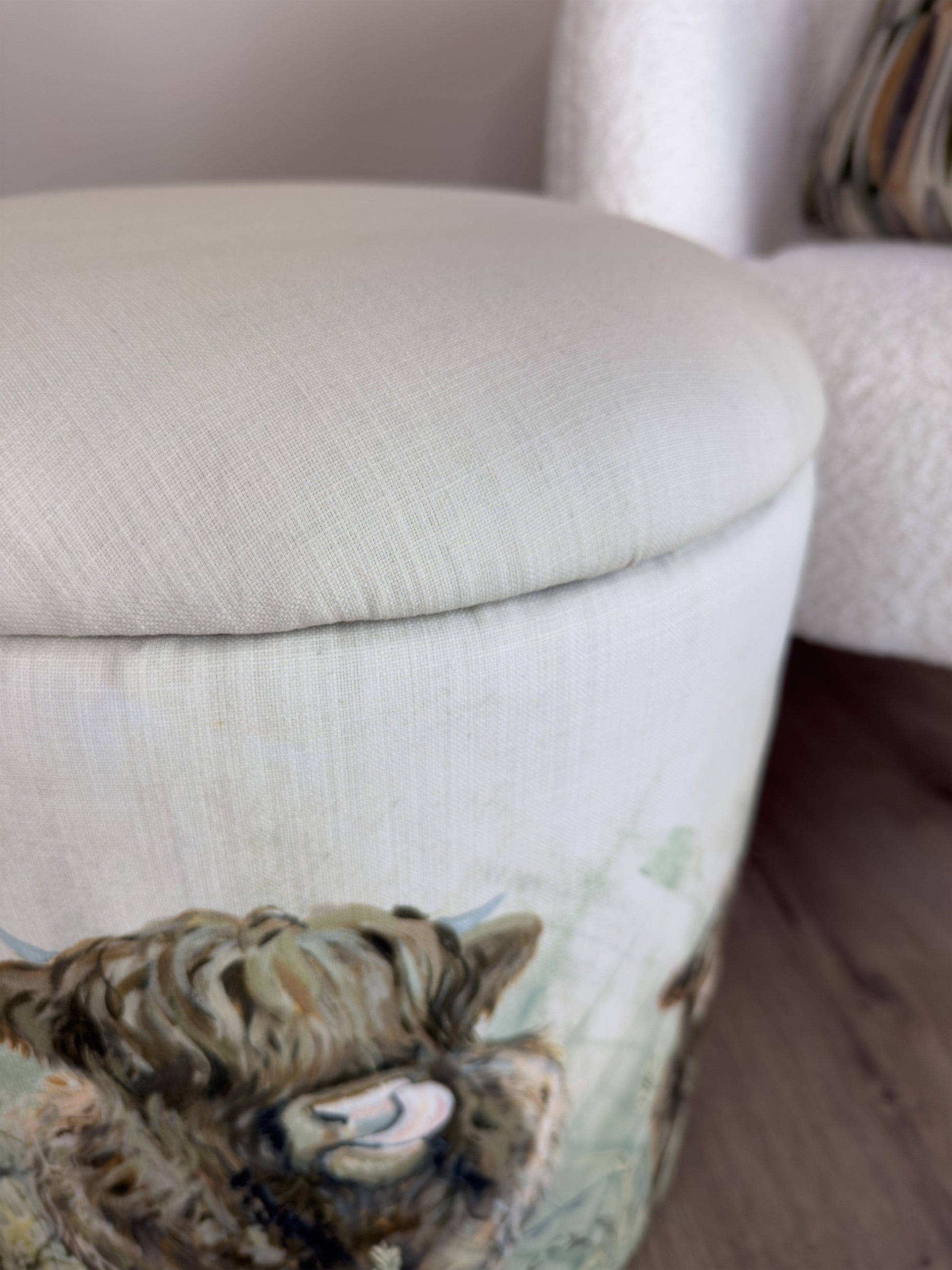 Close-up of a white linen ottoman with a decorative animal cow on a wooden floor.