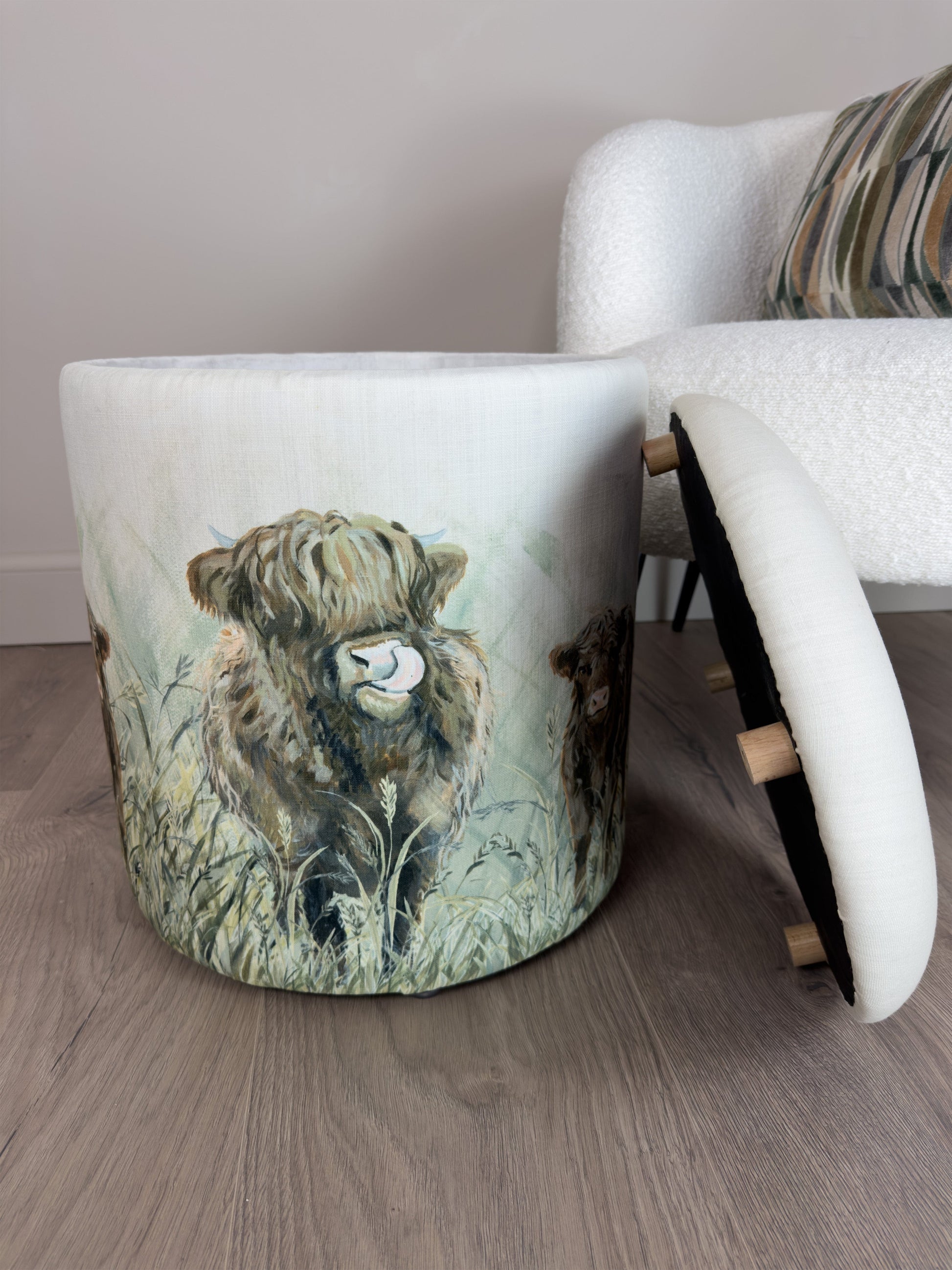 Stool with a highland cow design on a wooden floor next to a white chair.