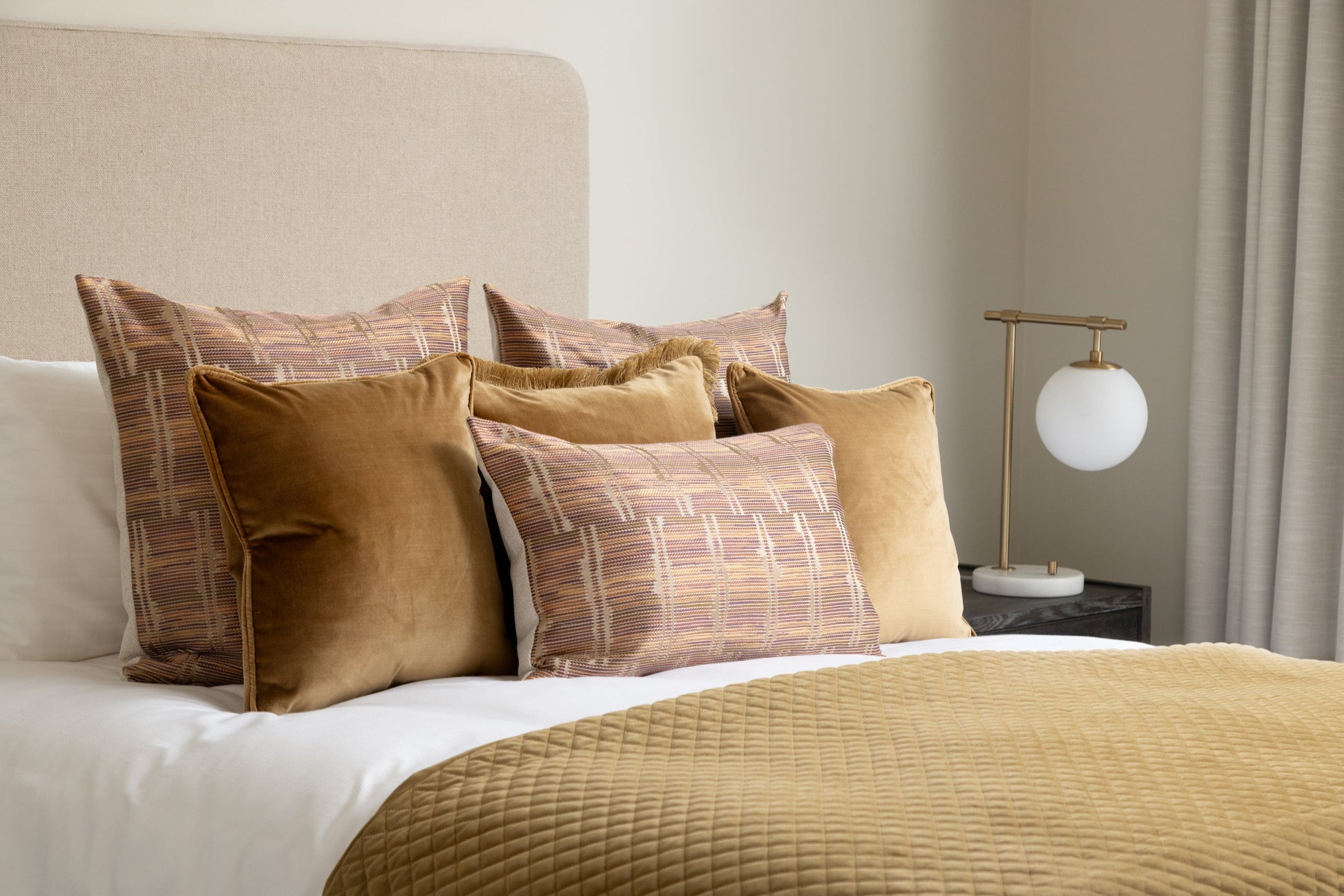 Bed with patterned pillows and a lamp on a nightstand in a bedroom setting.