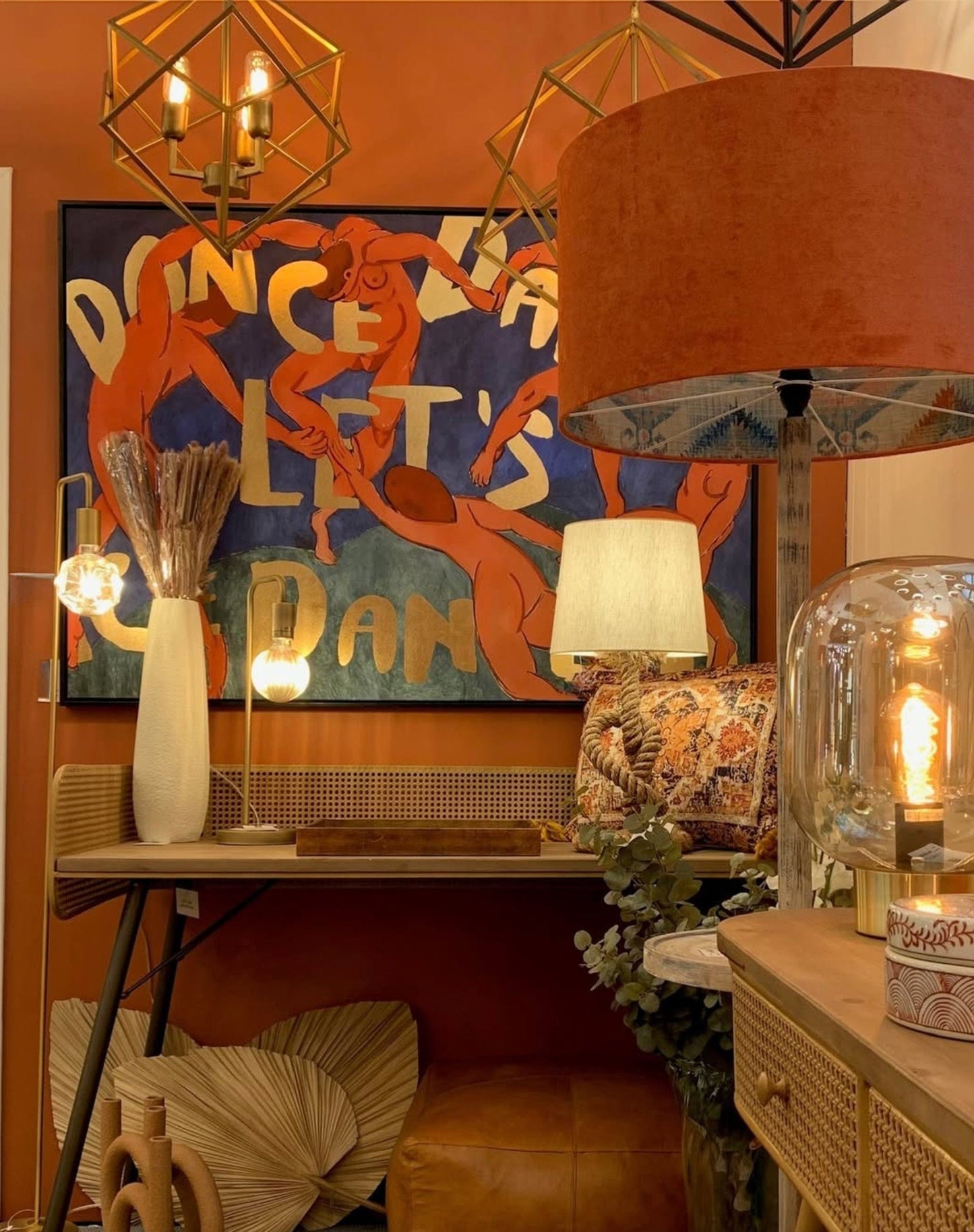 Decorative interior with a lamp, painting, and furniture against an orange wall.