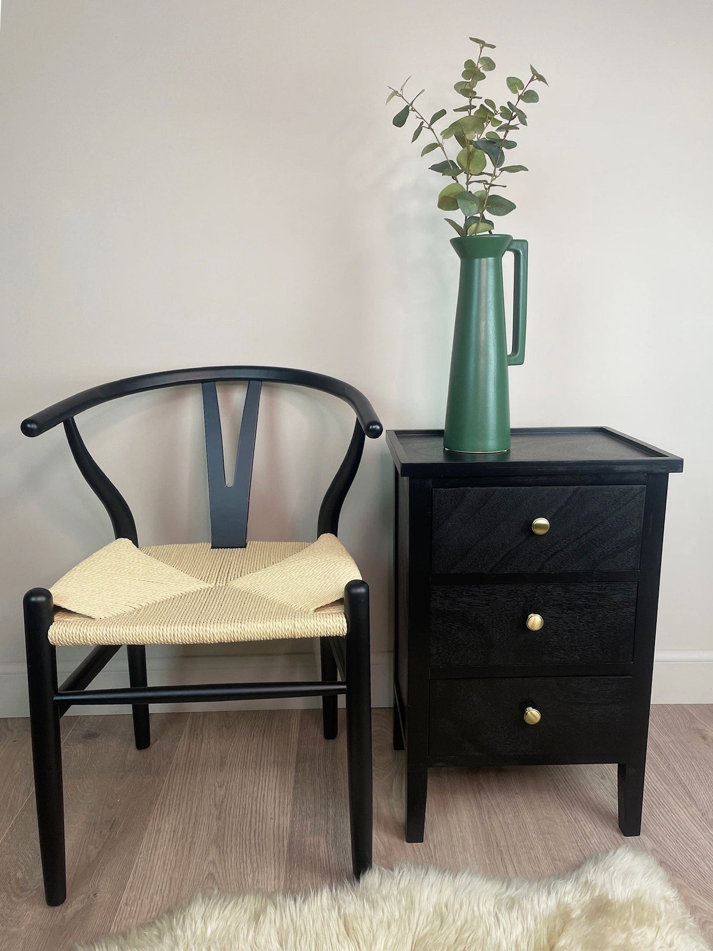 Black chair with woven seat next to a black nightstand with a green vase on a light wooden floor.