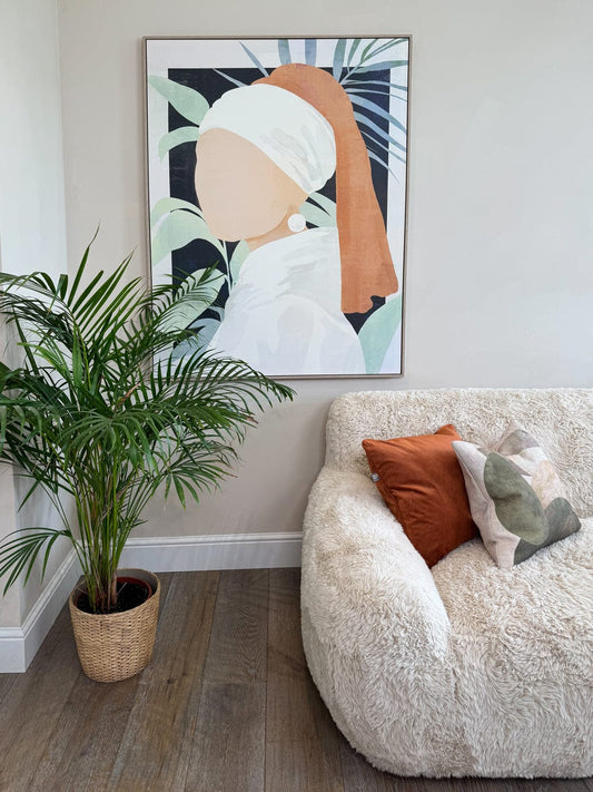 Living room with a beige armchair, plant, and wall art of a modern girl with a pearl earring