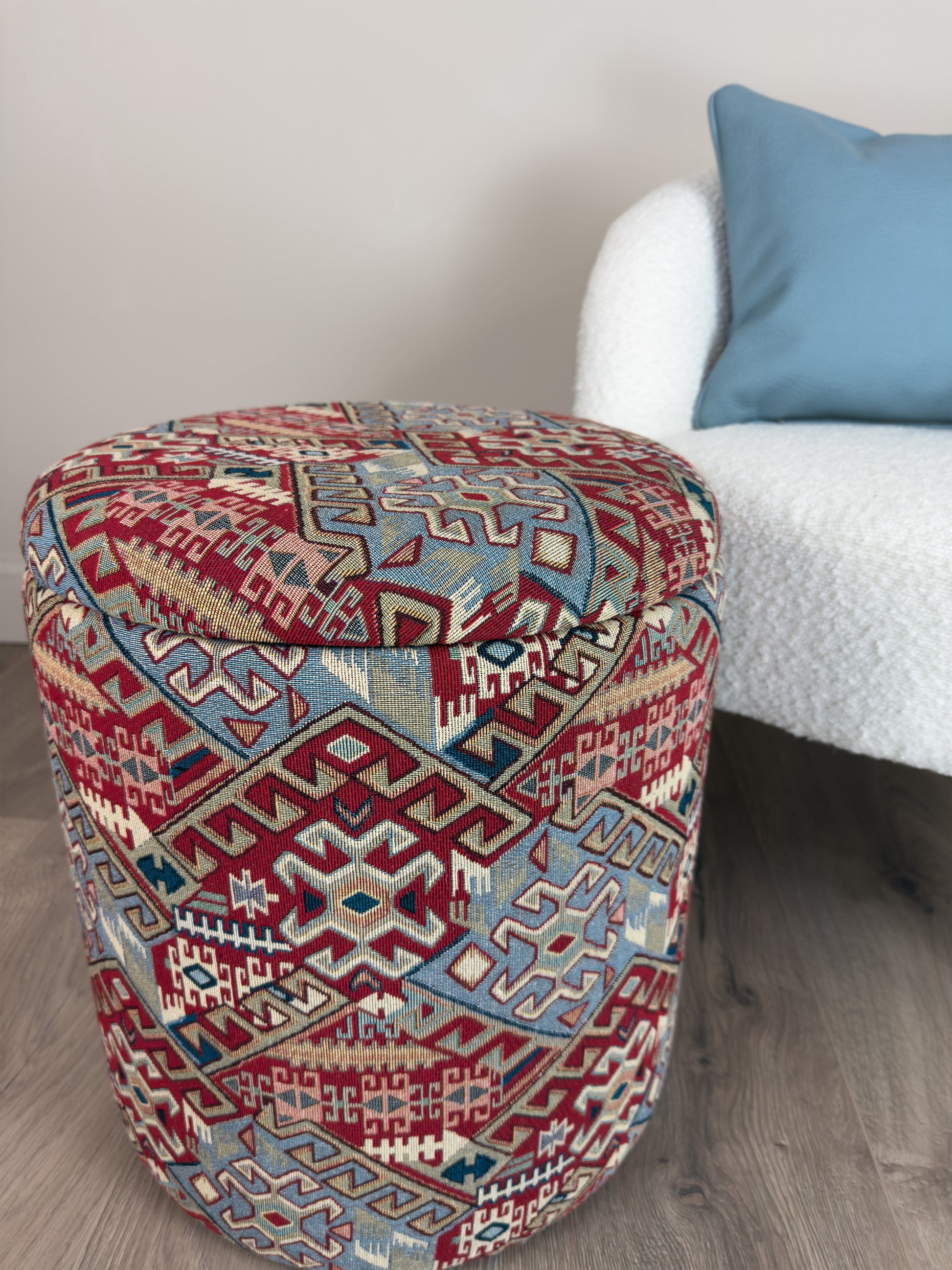 Decorative ottoman with geometric pattern next to a white chair with a blue pillow.