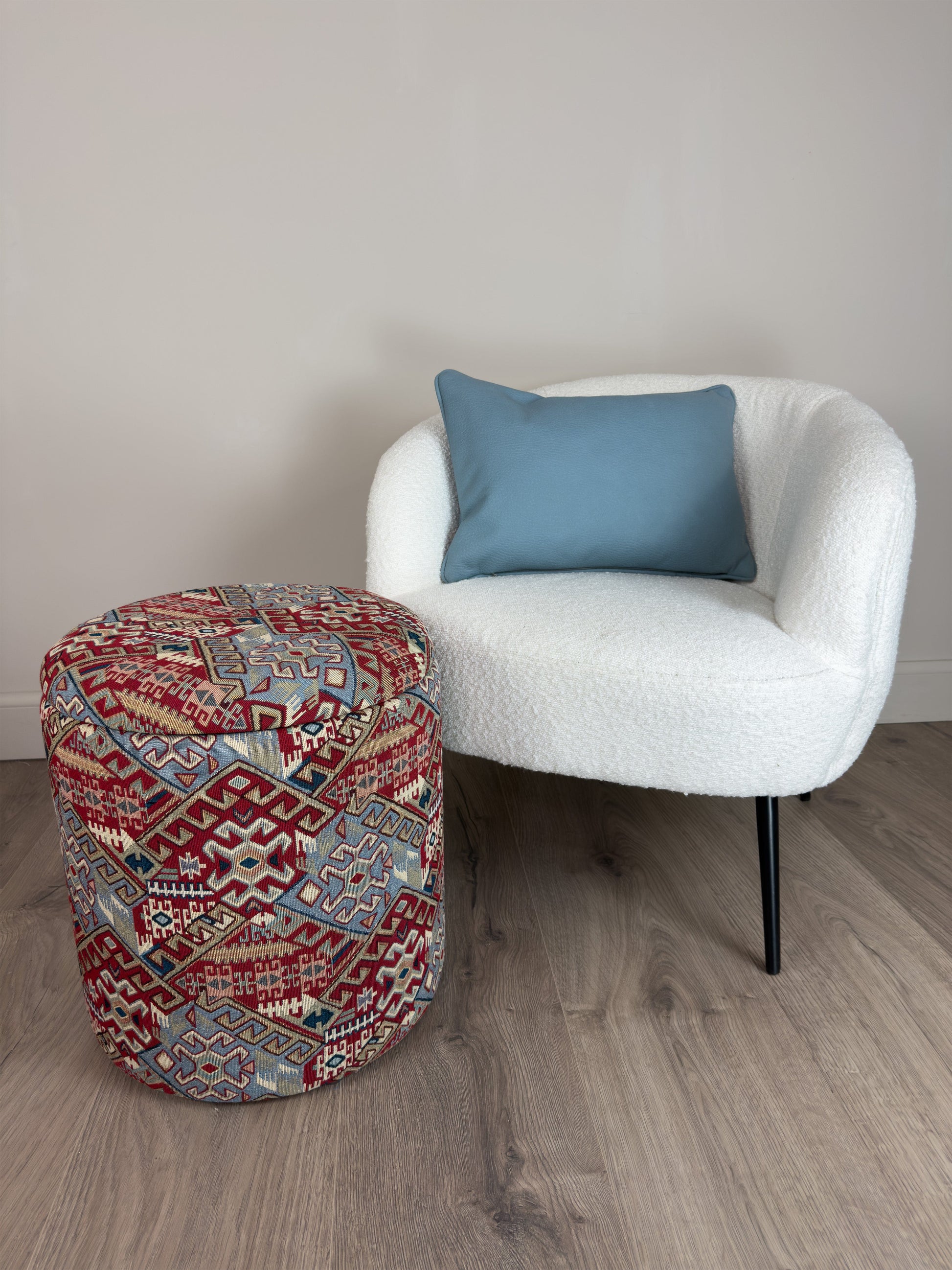 White chair with a blue pillow and a patterned ottoman on a wooden floor.