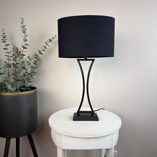 Black table lamp on a white round table with a plant in the background
