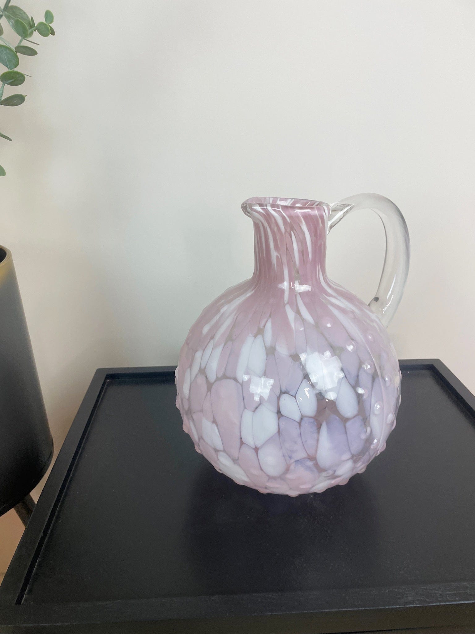 Pink glass pitcher on a dark surface with a light background