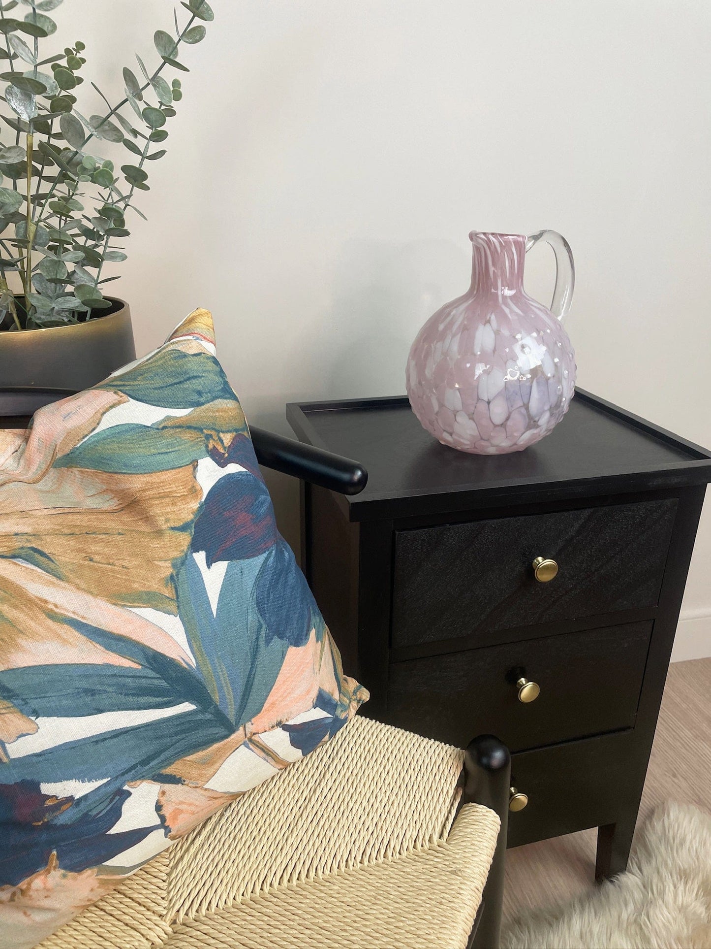 Black nightstand with a decorative pillow and vase, next to a plant.