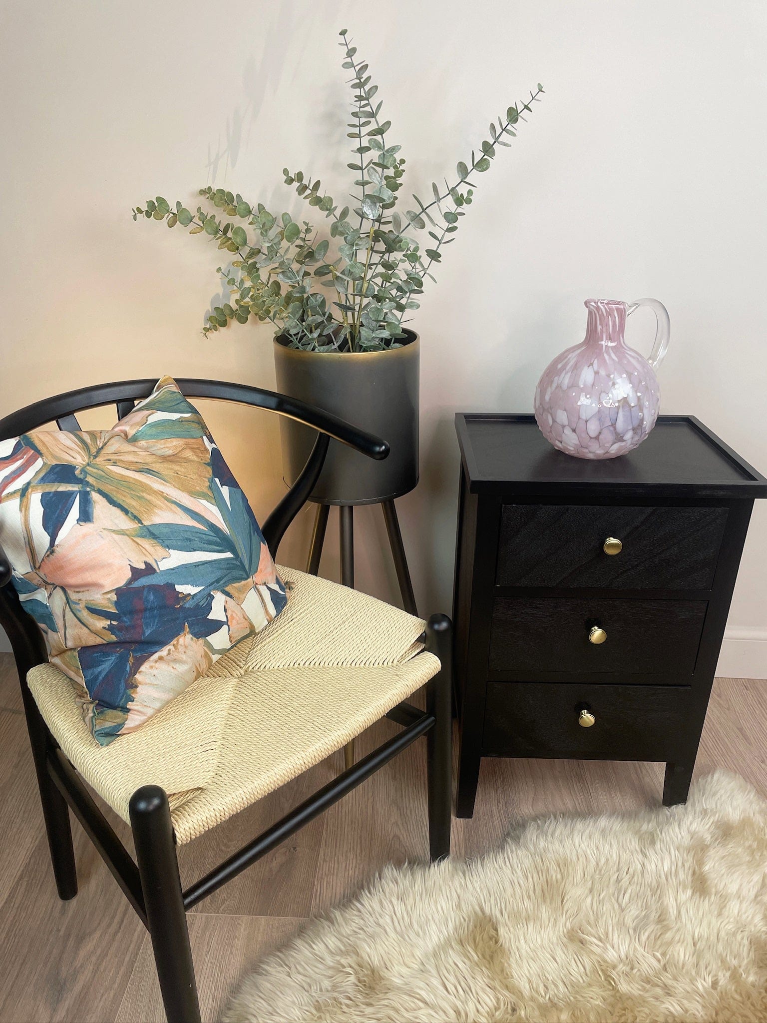 Chair with floral pillow and plant next to a black side table with a pink vase.