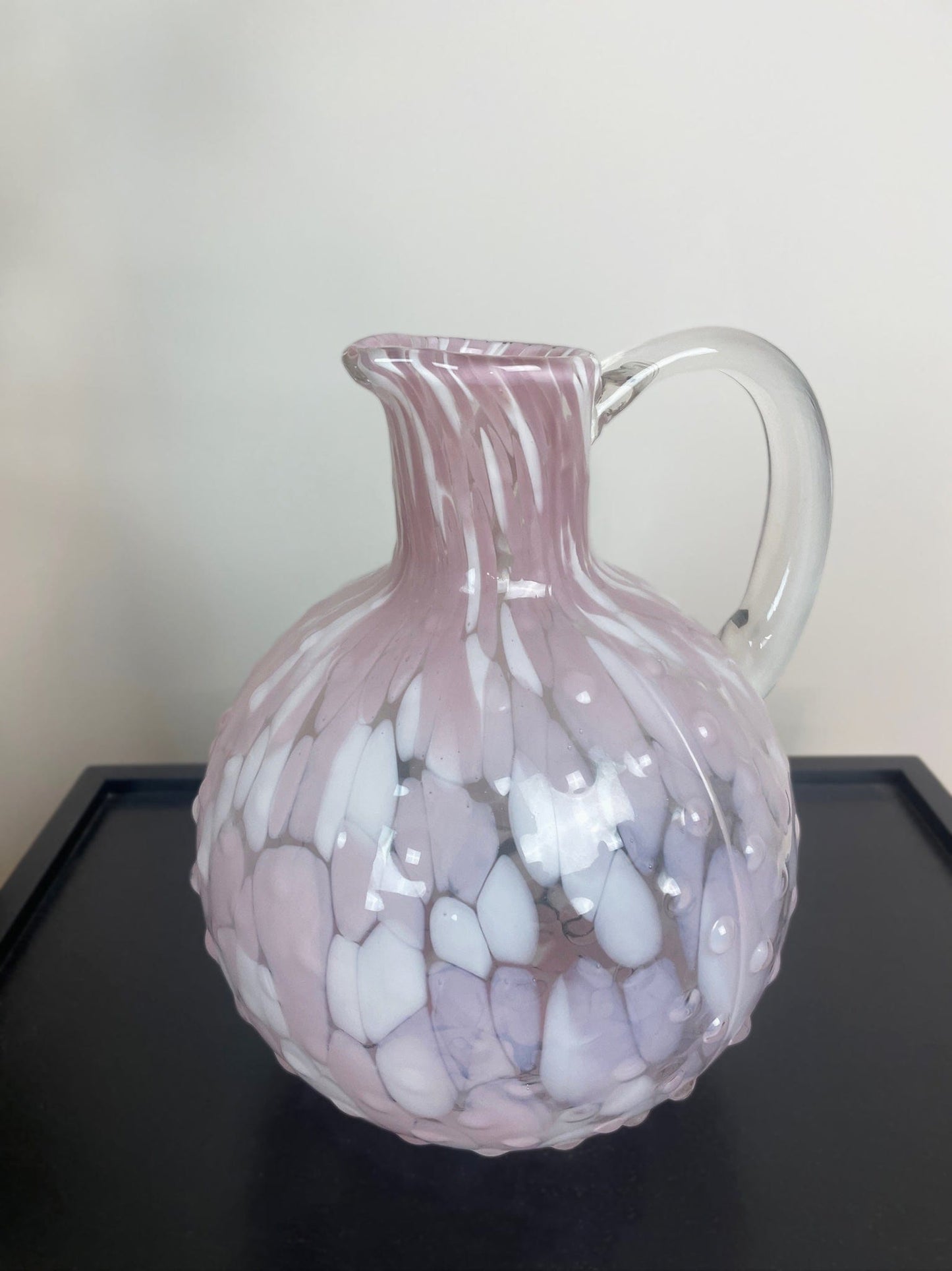 Pink glass pitcher with white marbled pattern on a black surface