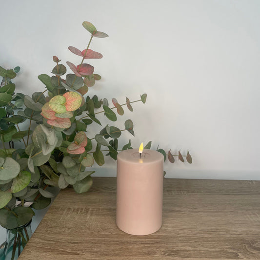 A pink LED candle placed on a wooden surface with a green plant in the background.
