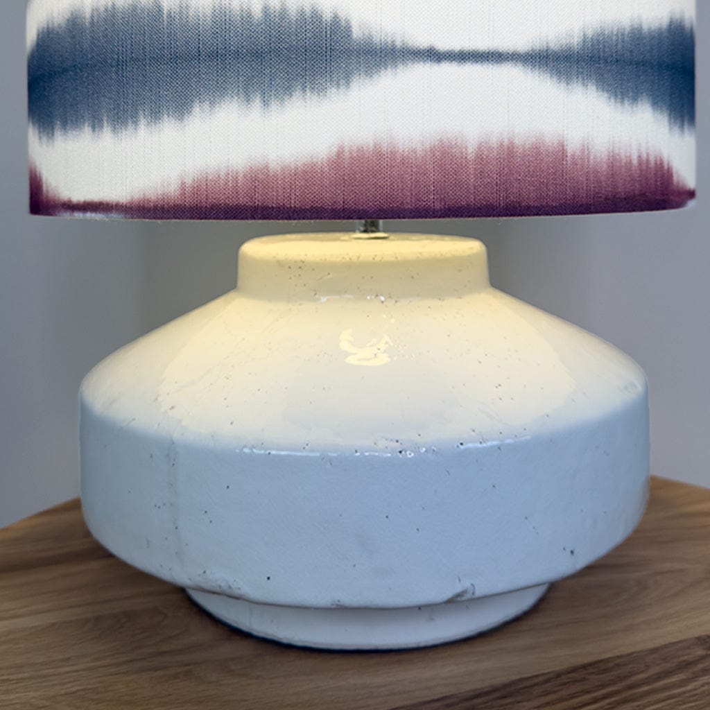 Table lamp with a textured white base and a colorful striped shade on a wooden surface.