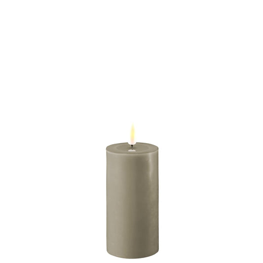 A sand-colored LED candle pillar standing 10cm tall and 5cm wide, made of real wax, with a visible warm glow at the top mimicking a flame.