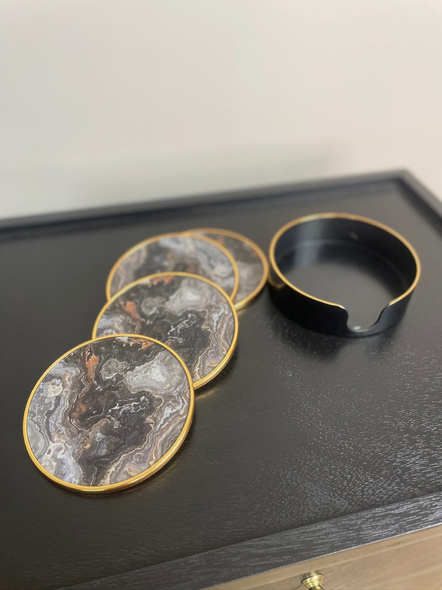 Set of marble-patterned coasters with a black circular dish on a dark surface.