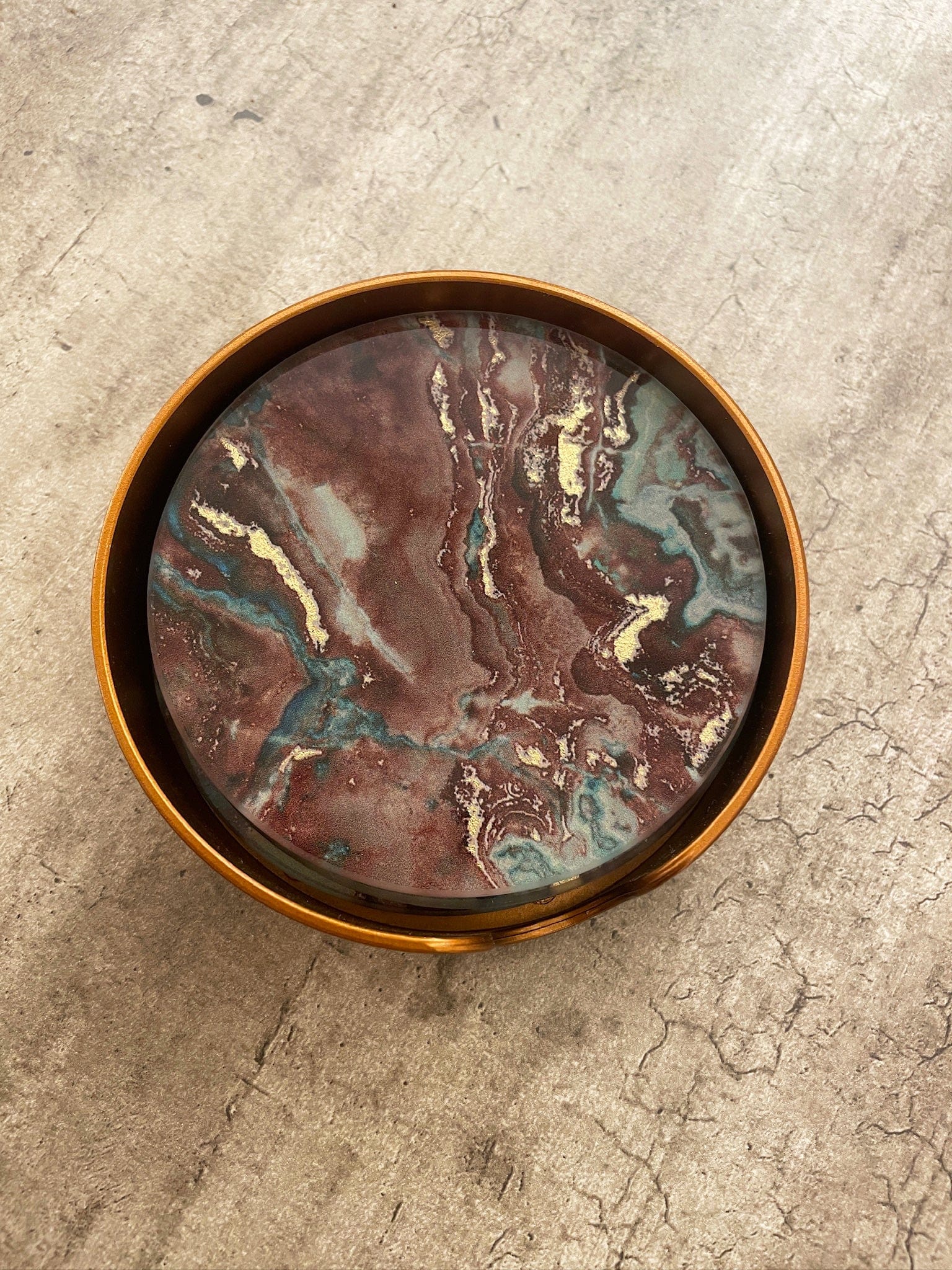 Marble-patterned coaster with bronze rim on a textured surface