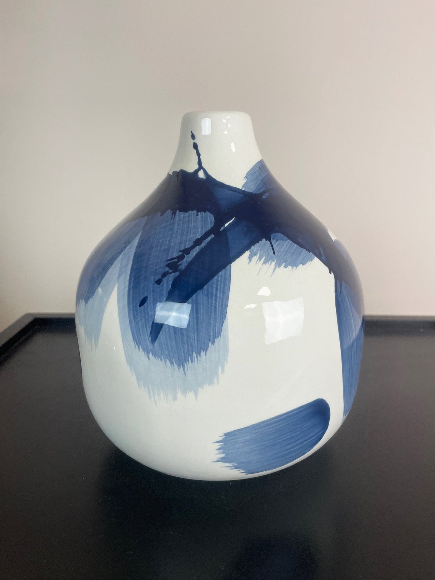 White vase with blue abstract patterns on a black surface and beige background