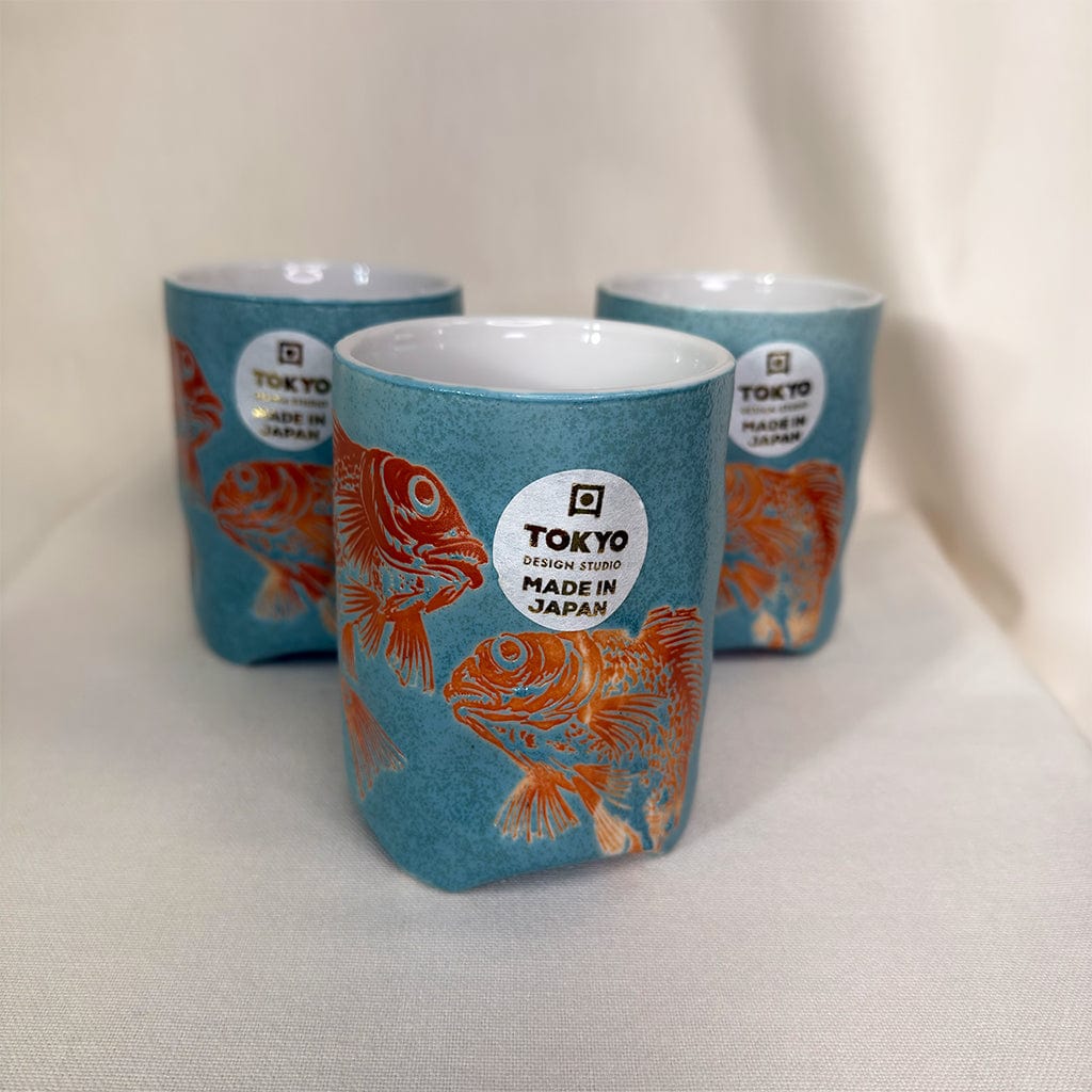 Three blue ceramic cups with orange fish design and 'Tokyo Design Studio Made in Japan' label on a white background.