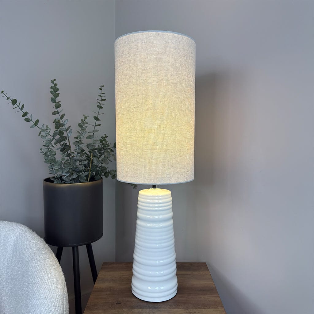 White textured table lamp on a wooden surface with a plant in the background