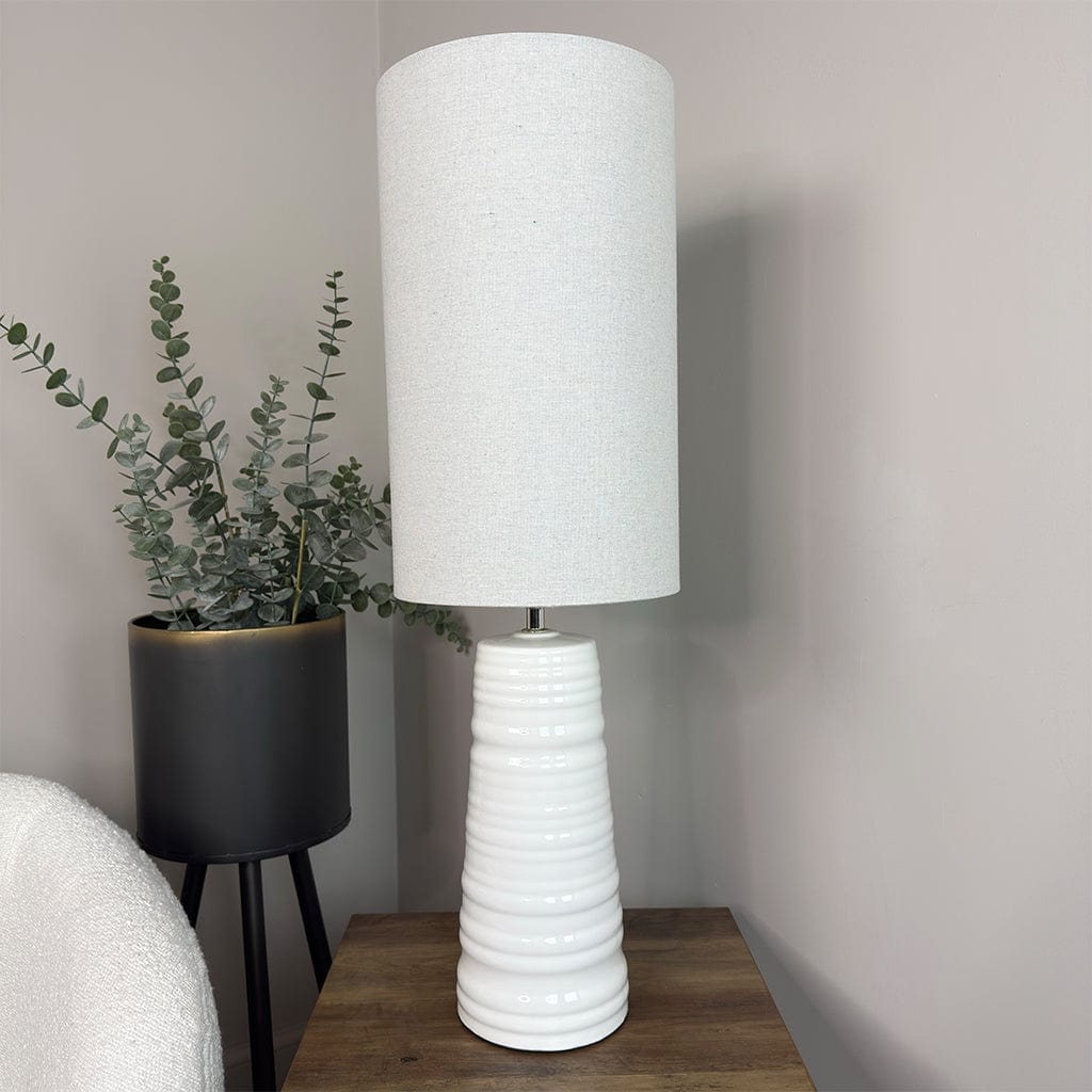 White textured table lamp on a wooden surface with a plant in the background
