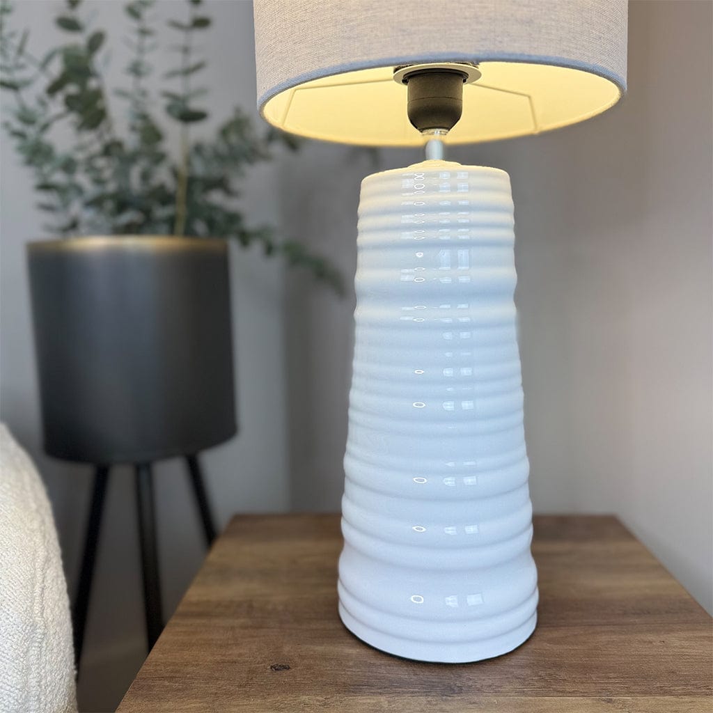 White textured table lamp on a wooden surface with a blurred plant in the background