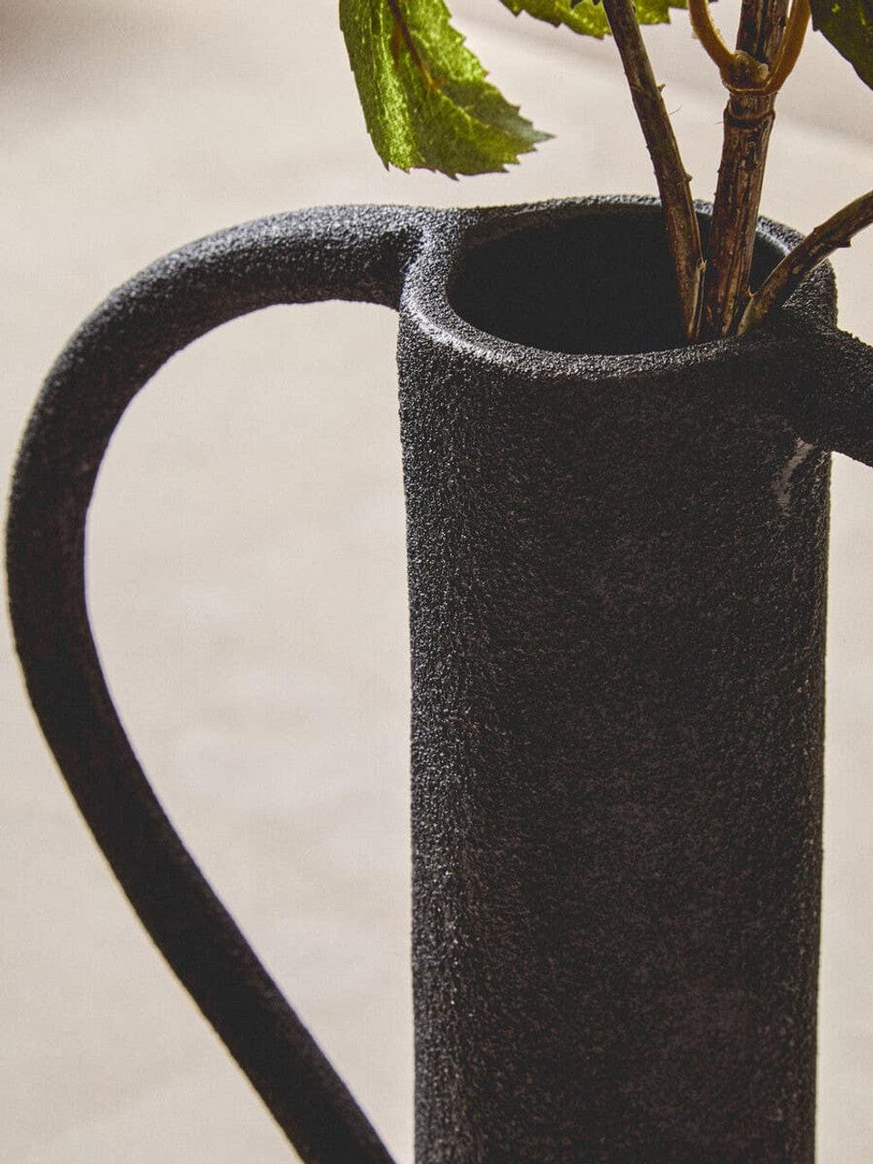 Black textured pitcher with a plant on a light background