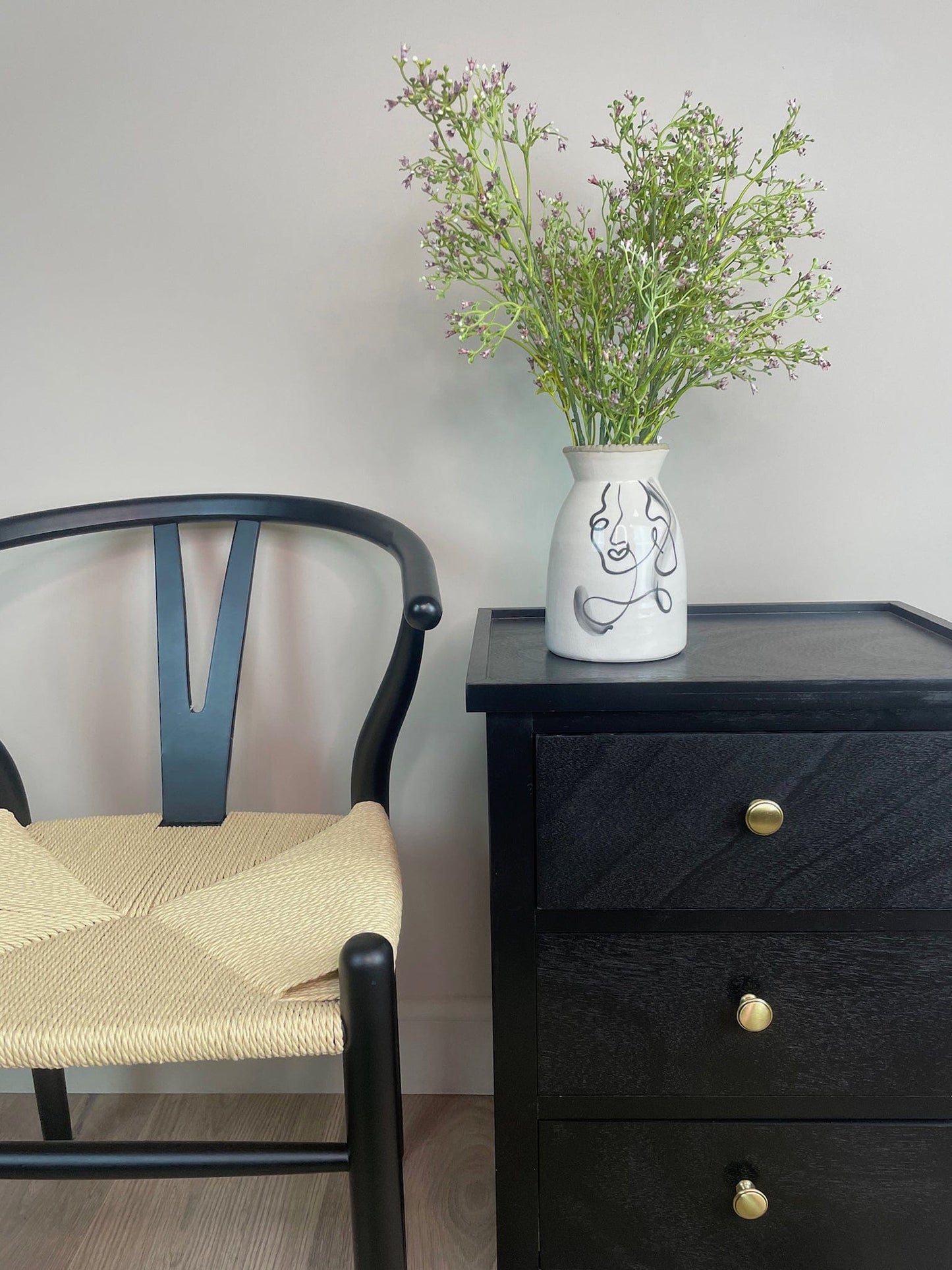 Black wooden drawer with a vase of flowers and a chair in a room.