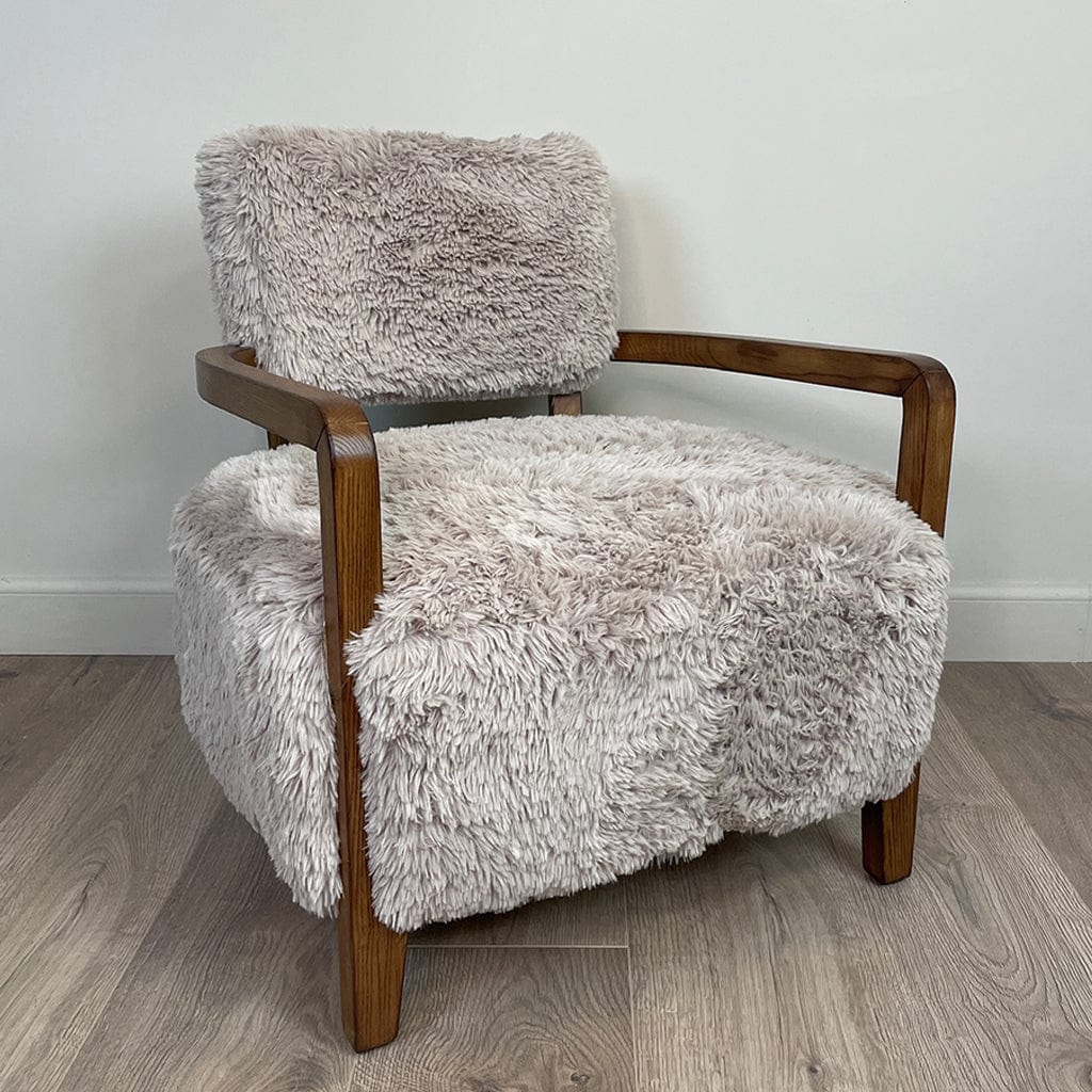 A caramel-colored faux fur armchair with dark ash wood arms, displayed in a cosy indoor setting.