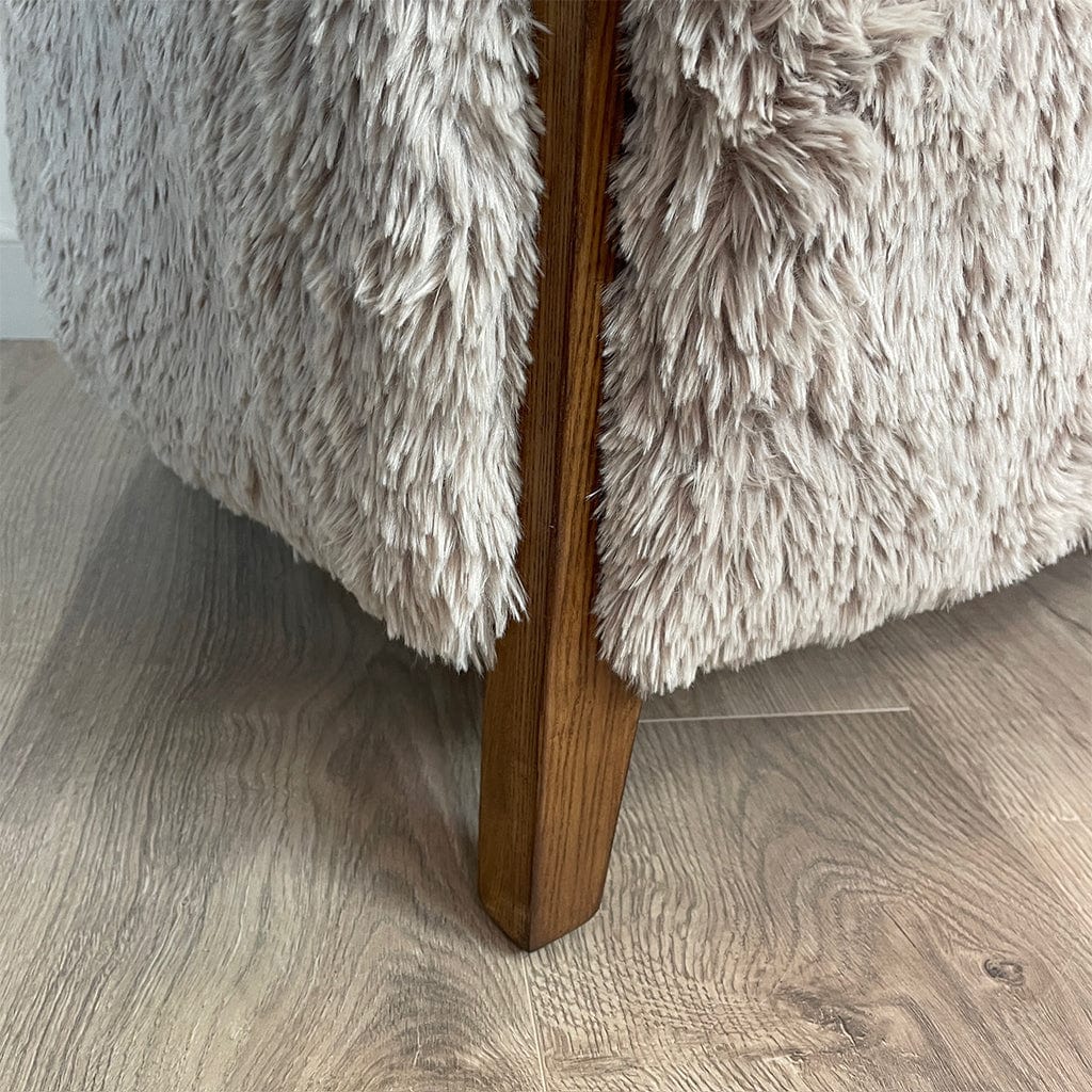 A caramel-colored faux fur armchair with dark ash wood legs, on a wooden floor.