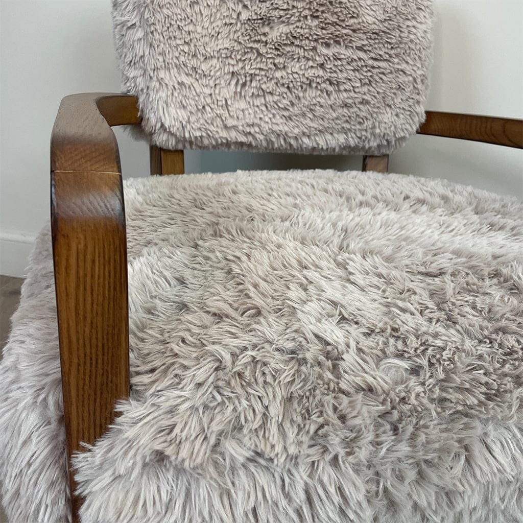 A caramel-colored faux fur armchair with dark ash wood arms, displayed in a cozy indoor setting.