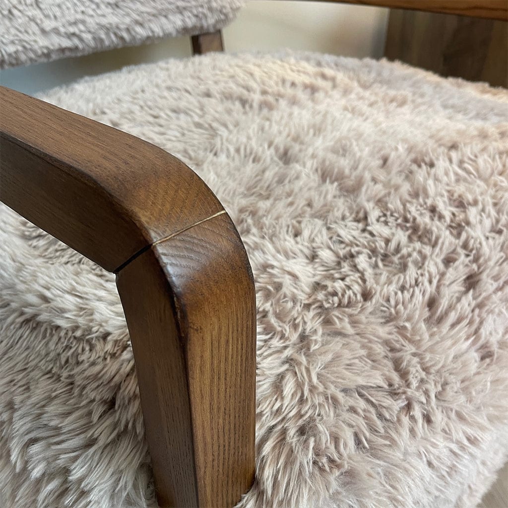 Close up caramel-colored faux fur armchair with dark ash wood arms, displayed in a cozy indoor setting.