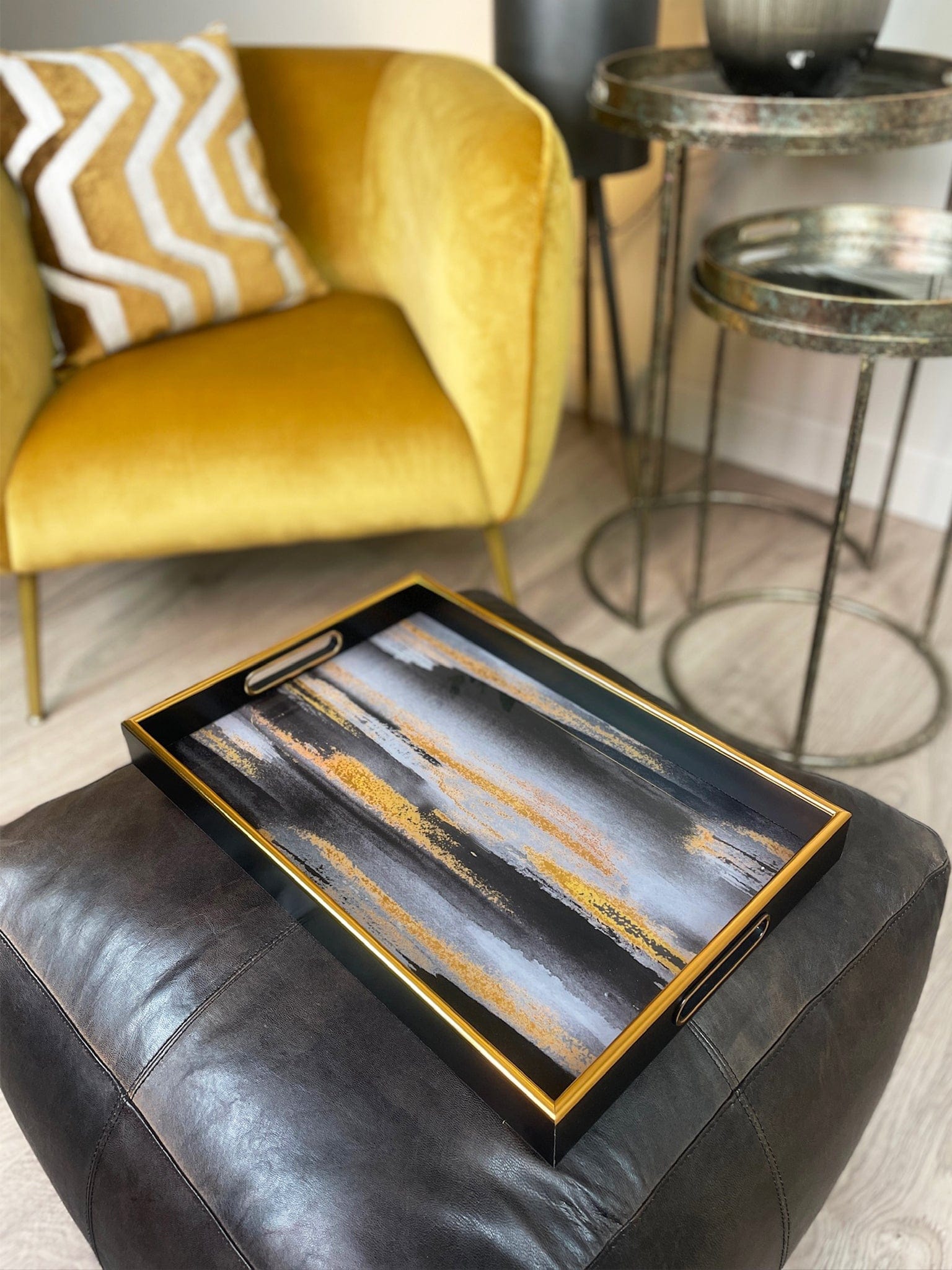 Decorative tray with abstract design on a black ottoman in a living room setting.