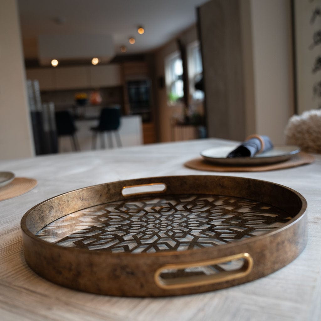 An antique gold mosaic tray with intricate patterns, placed on a table, with a blurred background showing a cozy room setting.