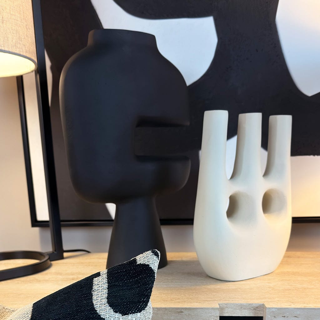 Two abstract vases, one black and one white, on a wooden surface with a lamp in the background.