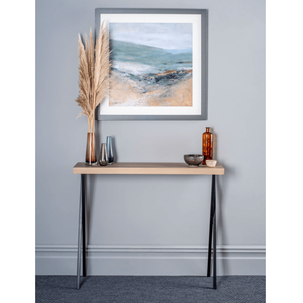 Console table with decorative items against a gray wall with a framed abstract painting.