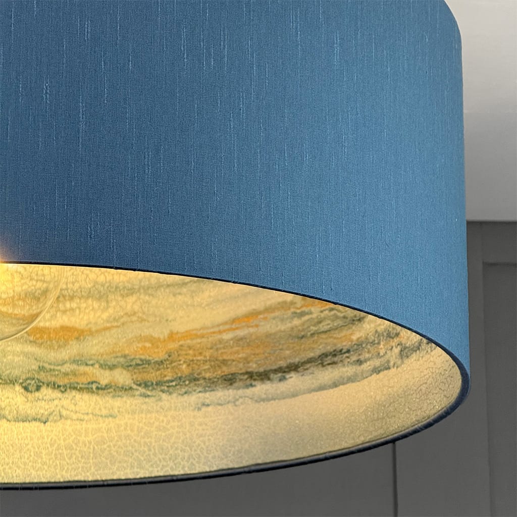 Close-up of a blue lampshade with a gold and green marble pattern on a gray surface.
