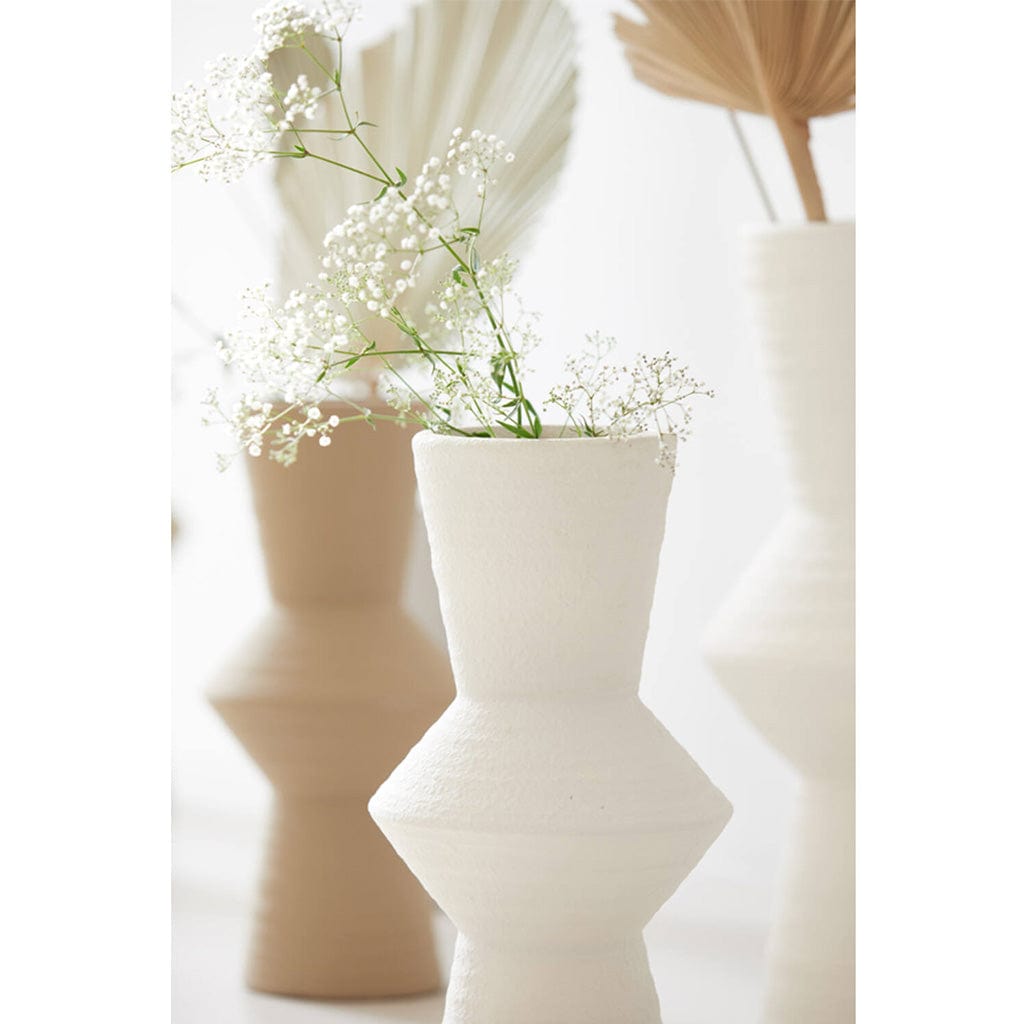 A sleek cream-colored ceramic vase with a geometric design, displayed with other vases in the background.
