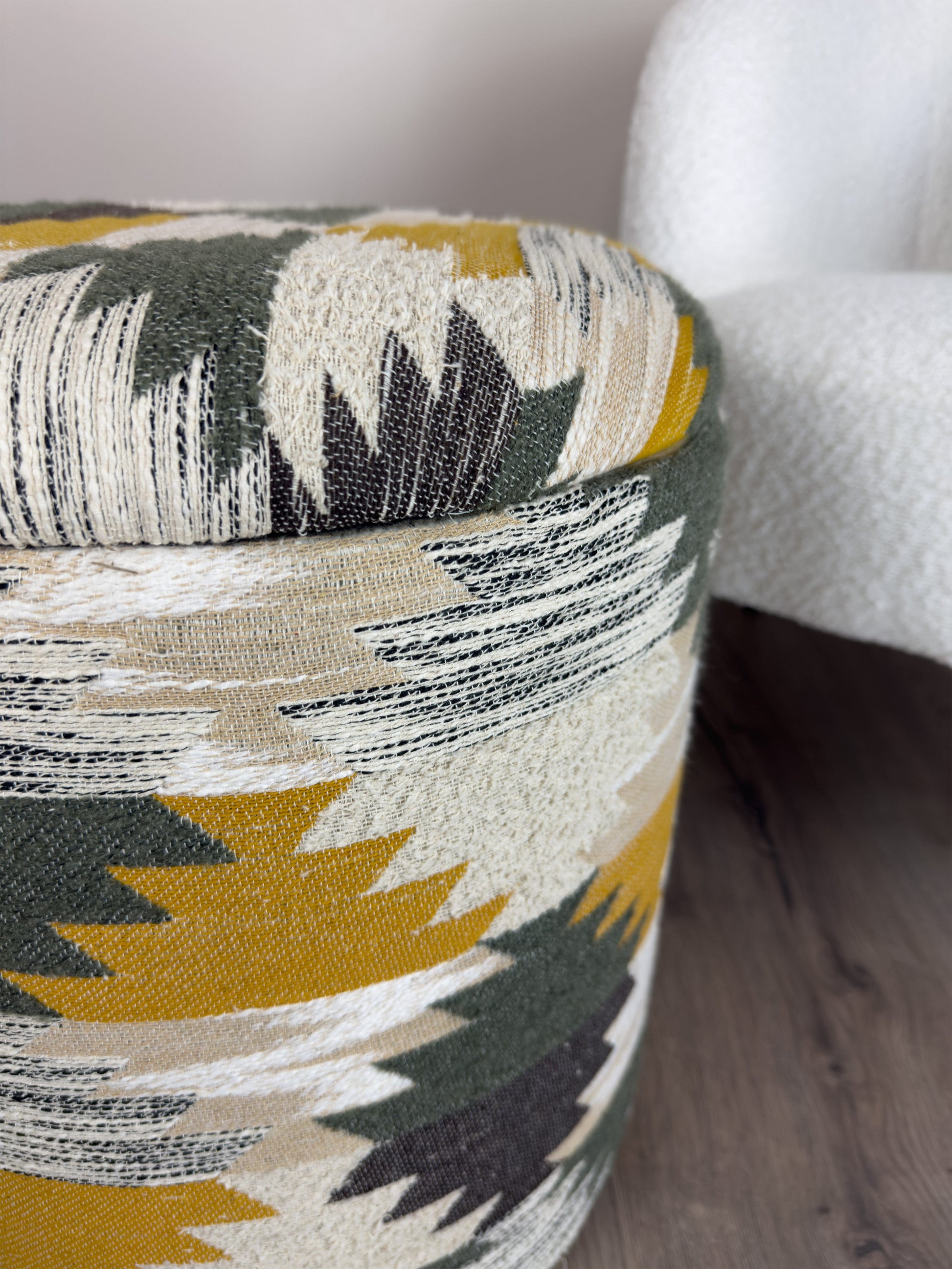 Patterned fabric storage footstool with geometric design on a wooden floor.